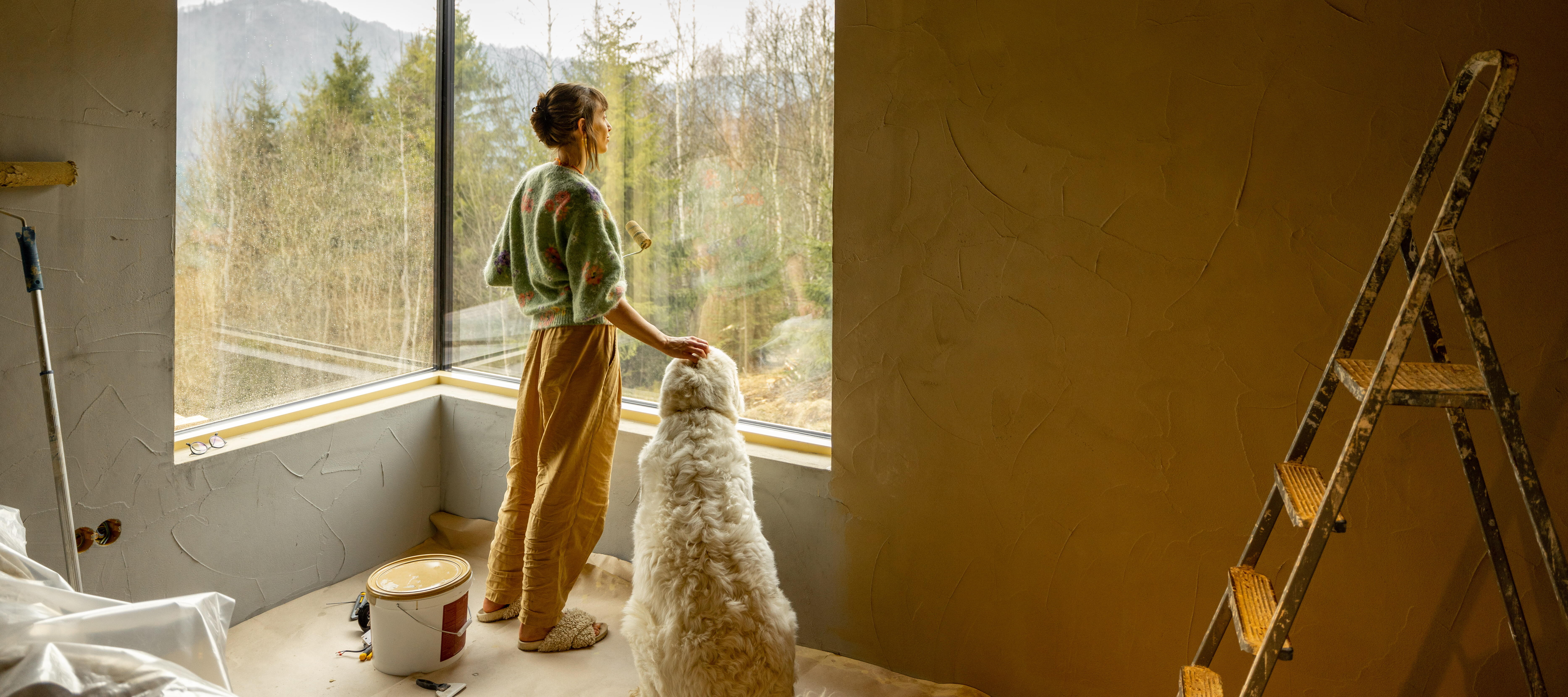 A woman takes a break from painting her home to look out the window.