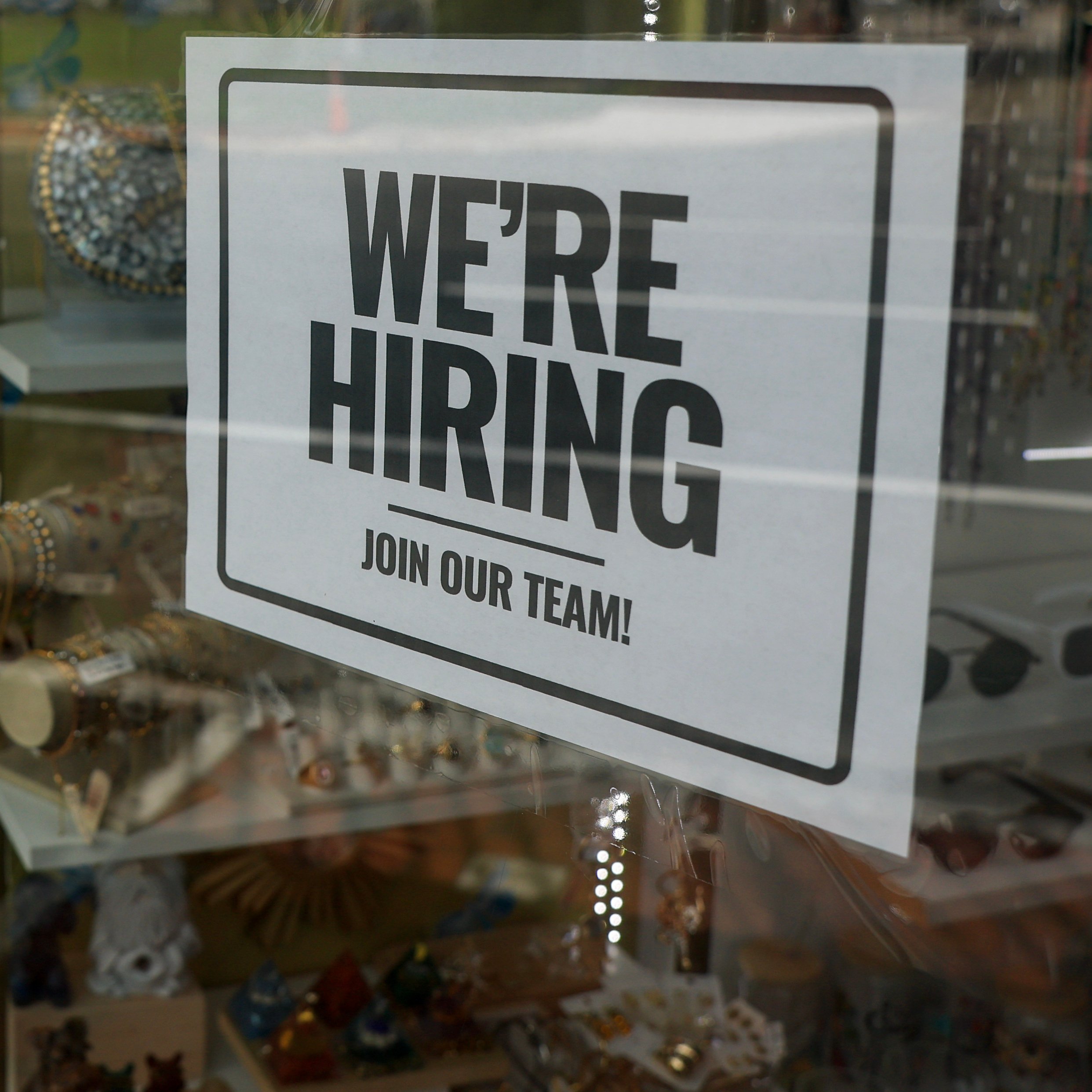 Two people walk by a store with a help wanted sign in the window.