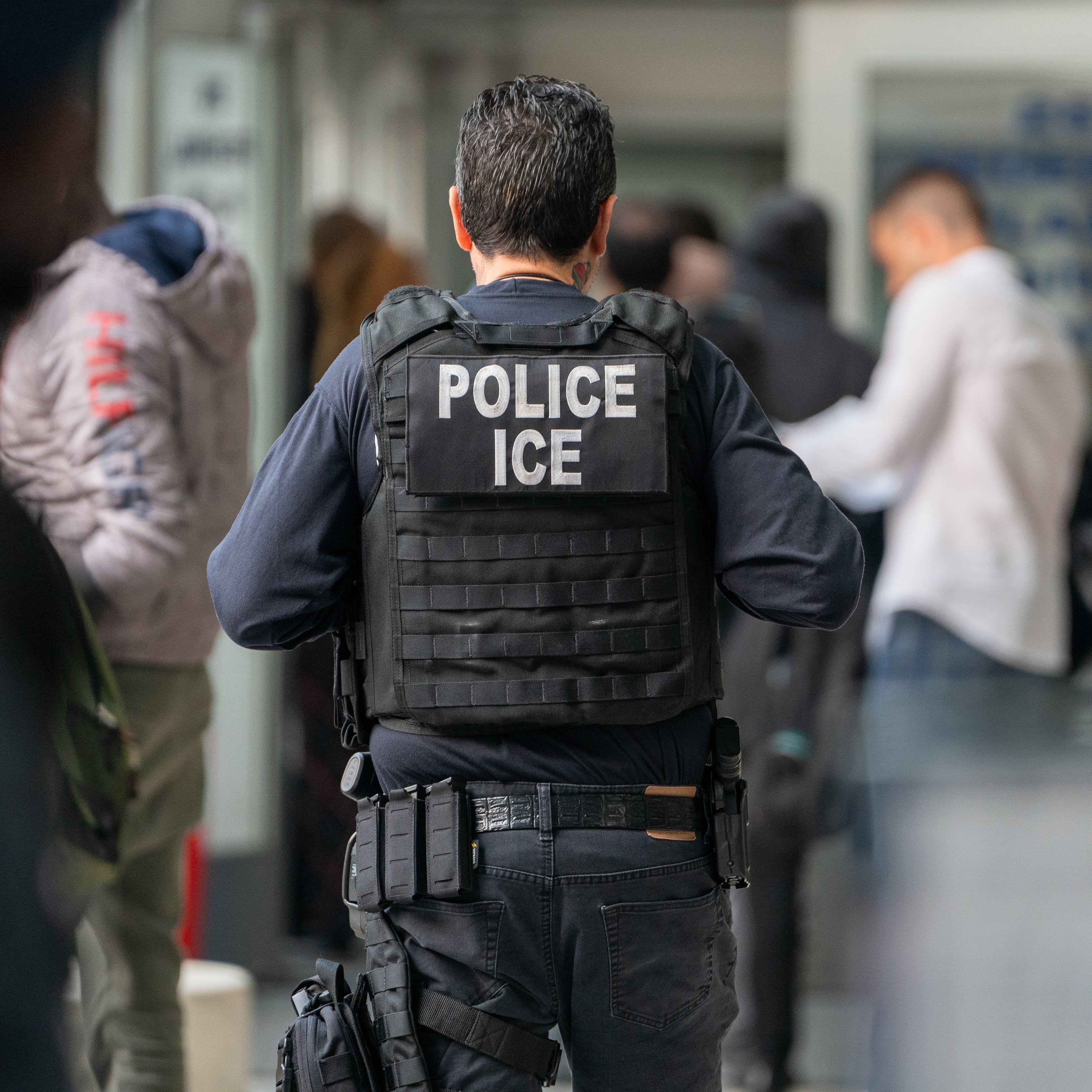 View from behind of an ICE agent monitors hundreds of asylum seekers being processed upon entering the Jacob K. Javits Federal Building