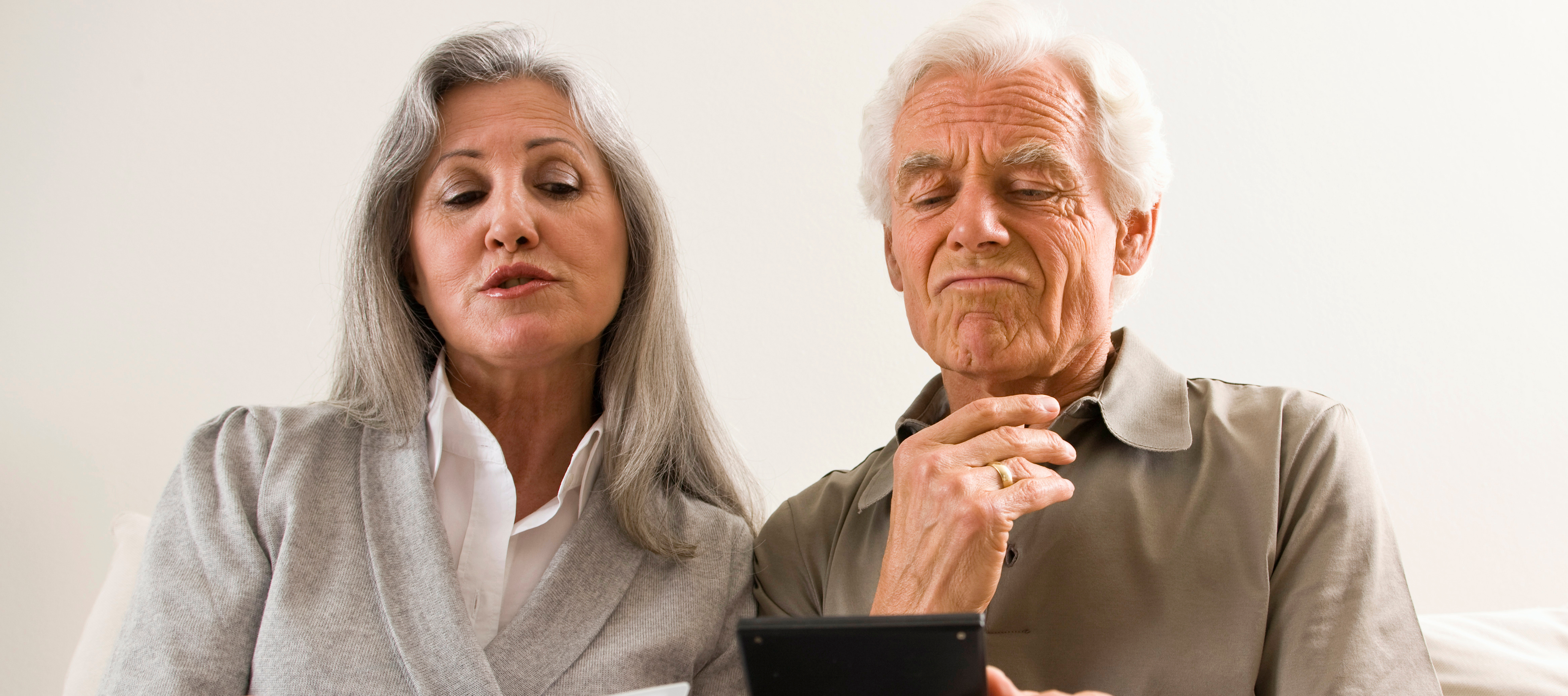 An older couple sitting together on a couch looking through a binder, holding a calculator.