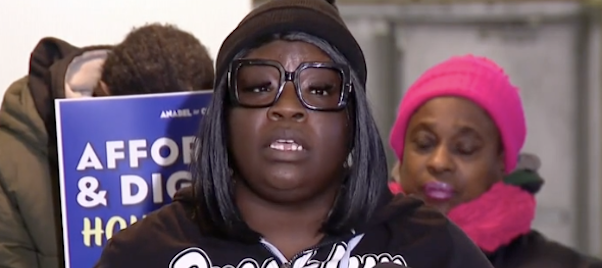 A resident at Chicago's Harrison Courts apartments in East Garfield Park holds a sign saying "Affordable & Dignified Housing Now!"