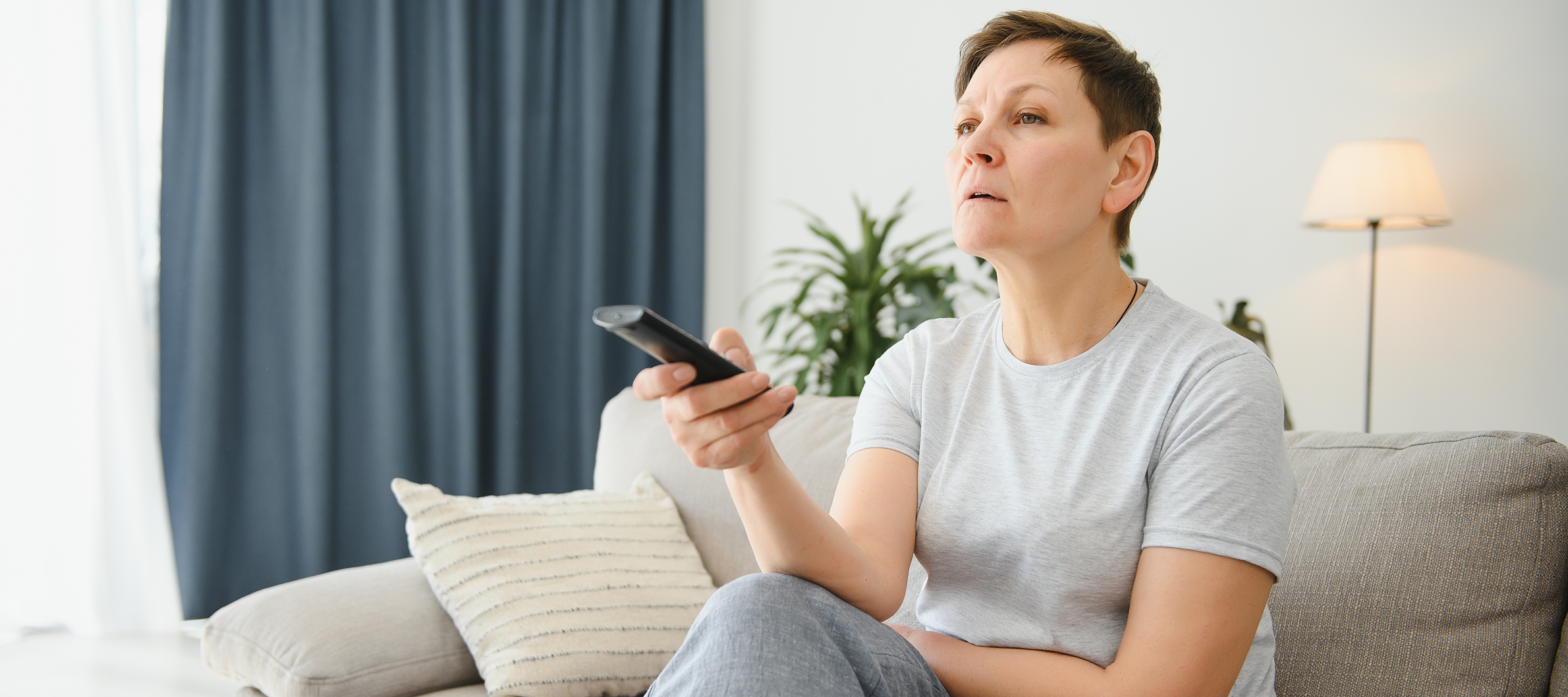 A concerned woman watches TV while holding the remote control.