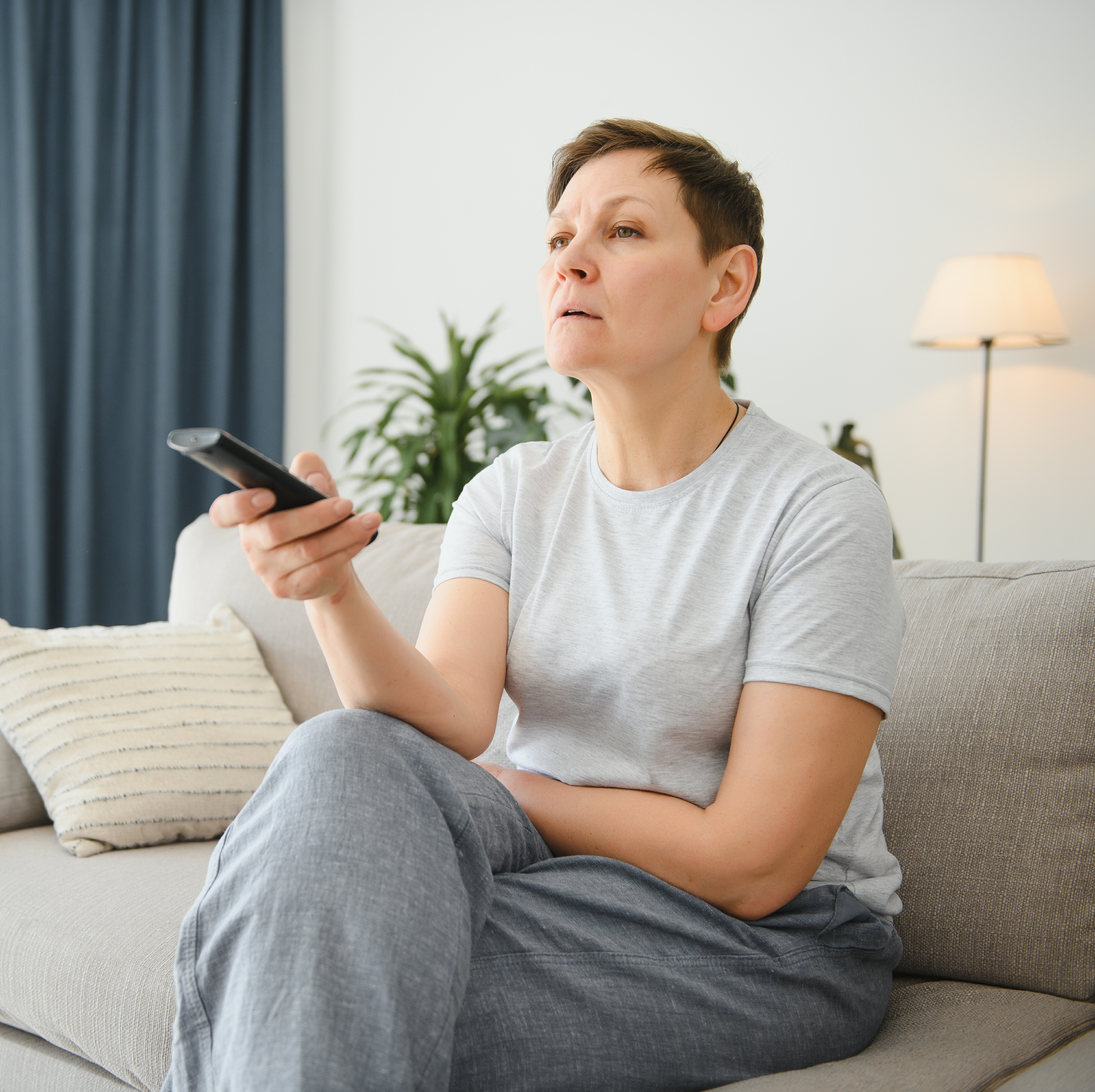 A concerned woman watches TV while holding the remote control.