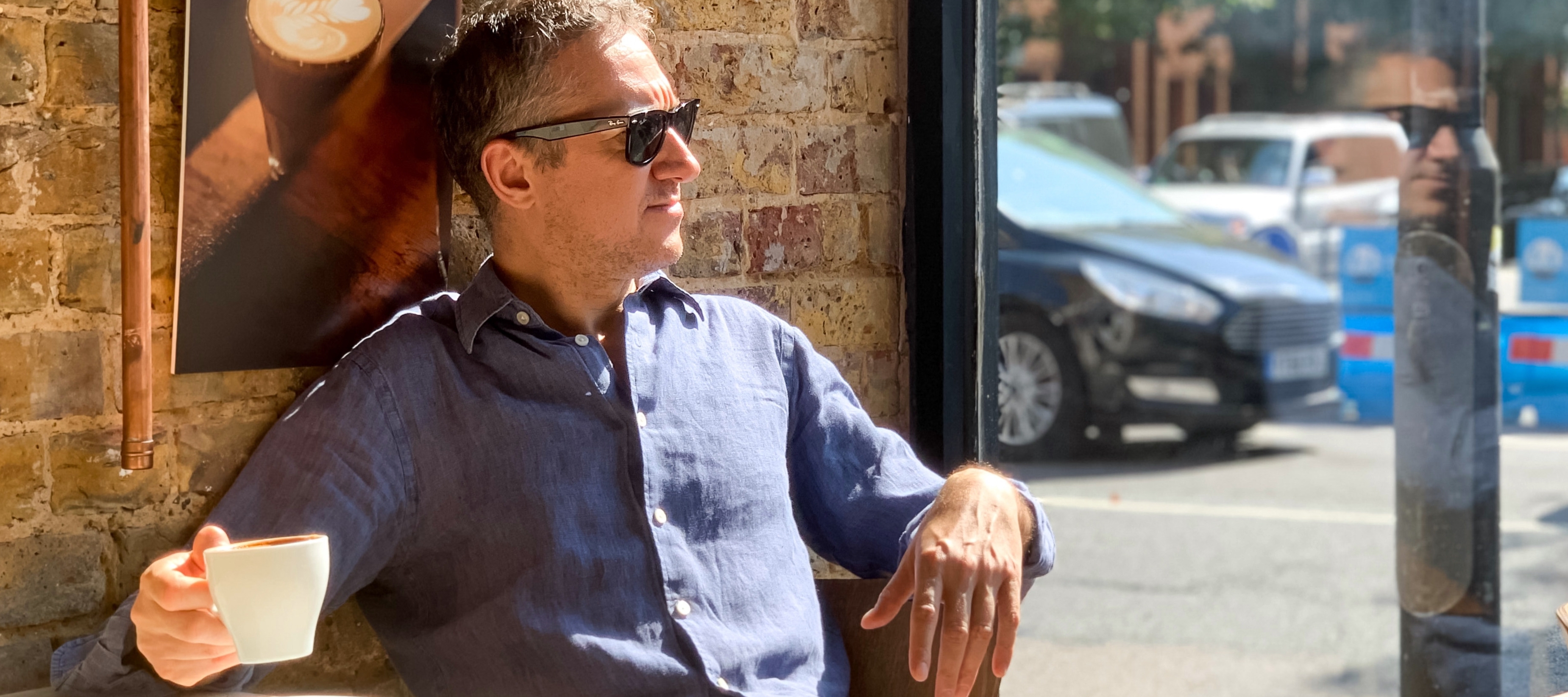 50 year old man thoughtfully drinking coffee in window of coffee shop.