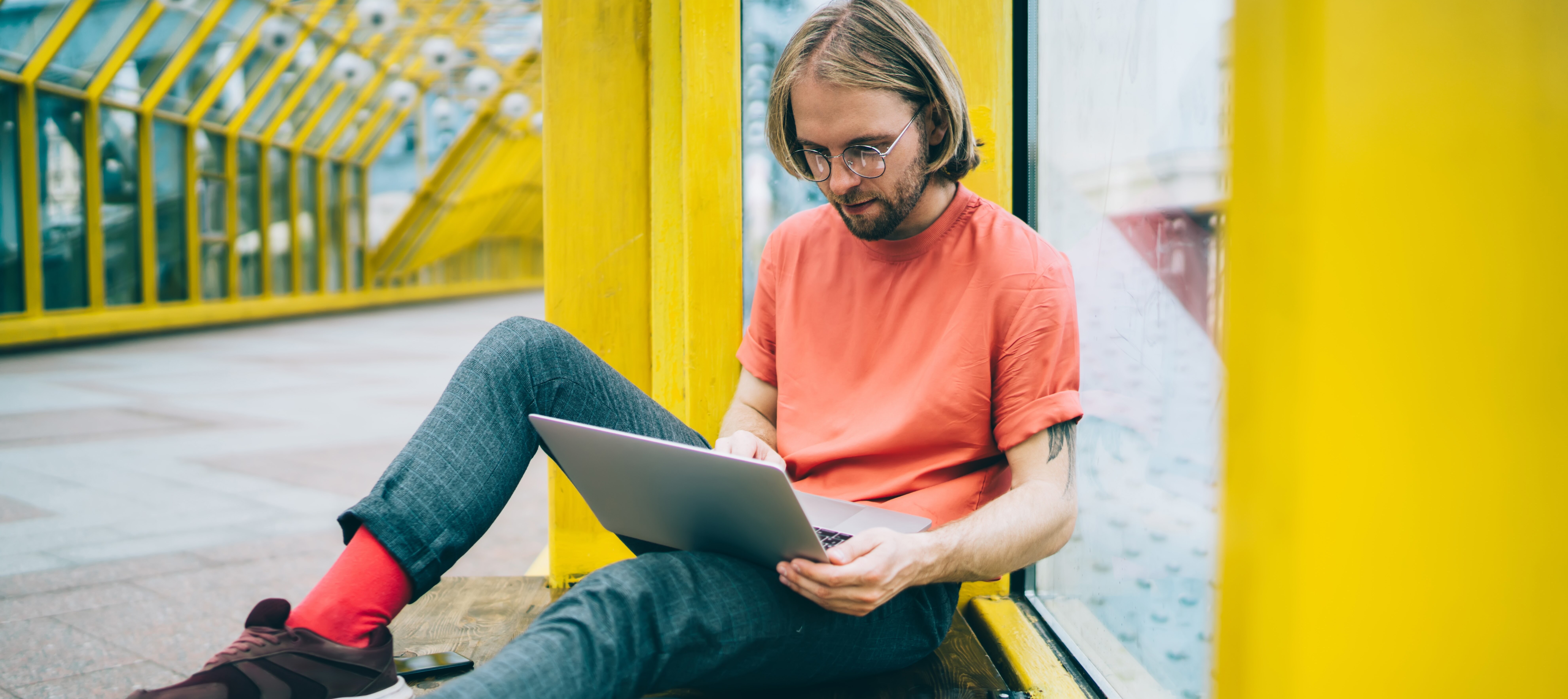 Young man doing freelance work on laptop in pedestrian bridge.