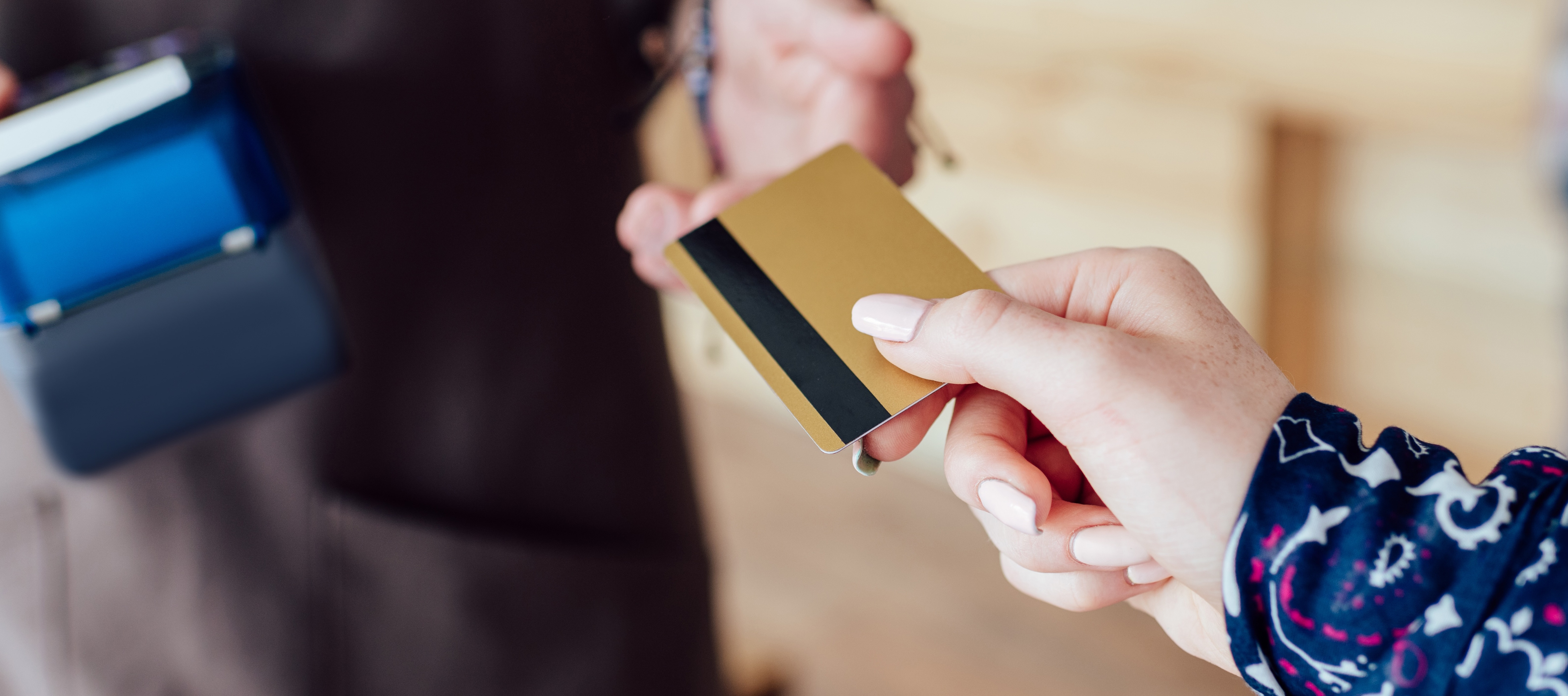 Close up of a person handing their card over to be used for tap payment against a handheld terminal.