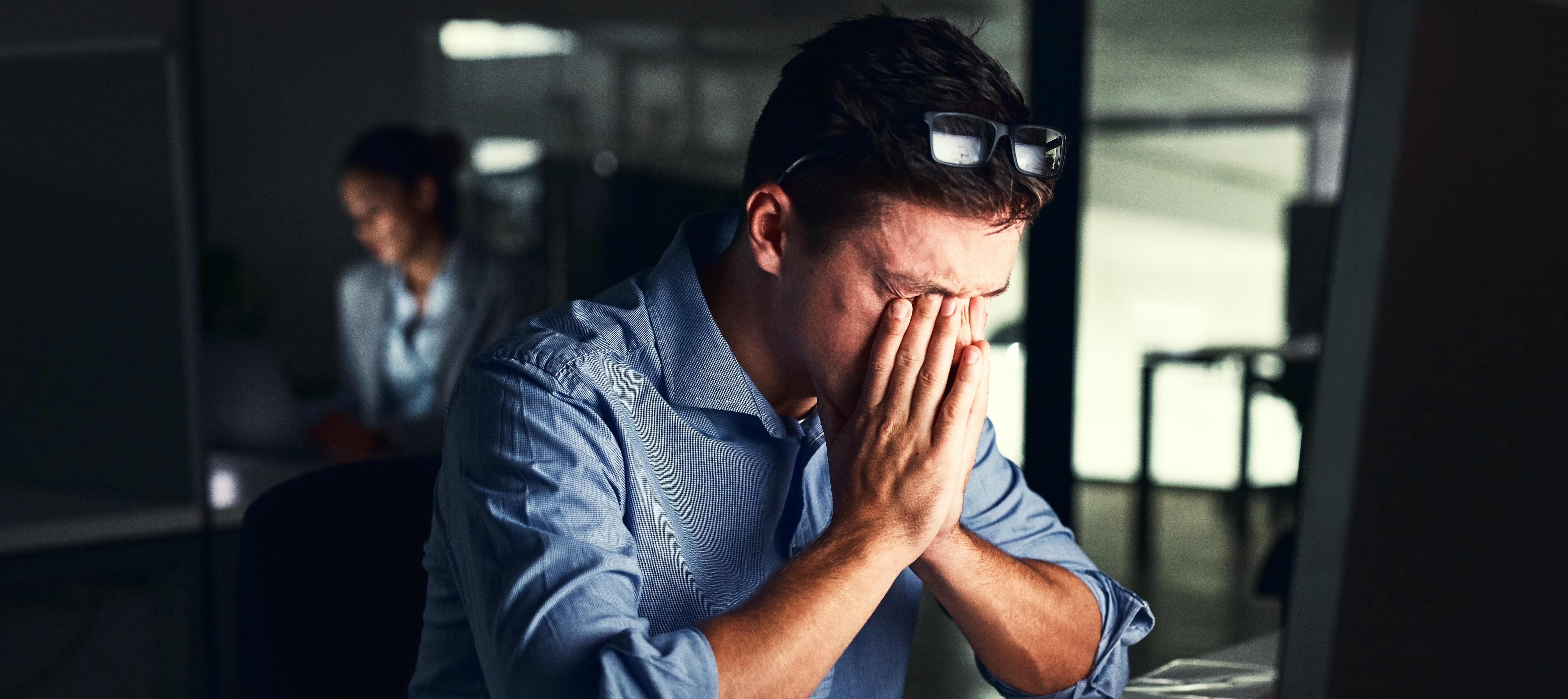 A tired man rubs his eyes at his desk.