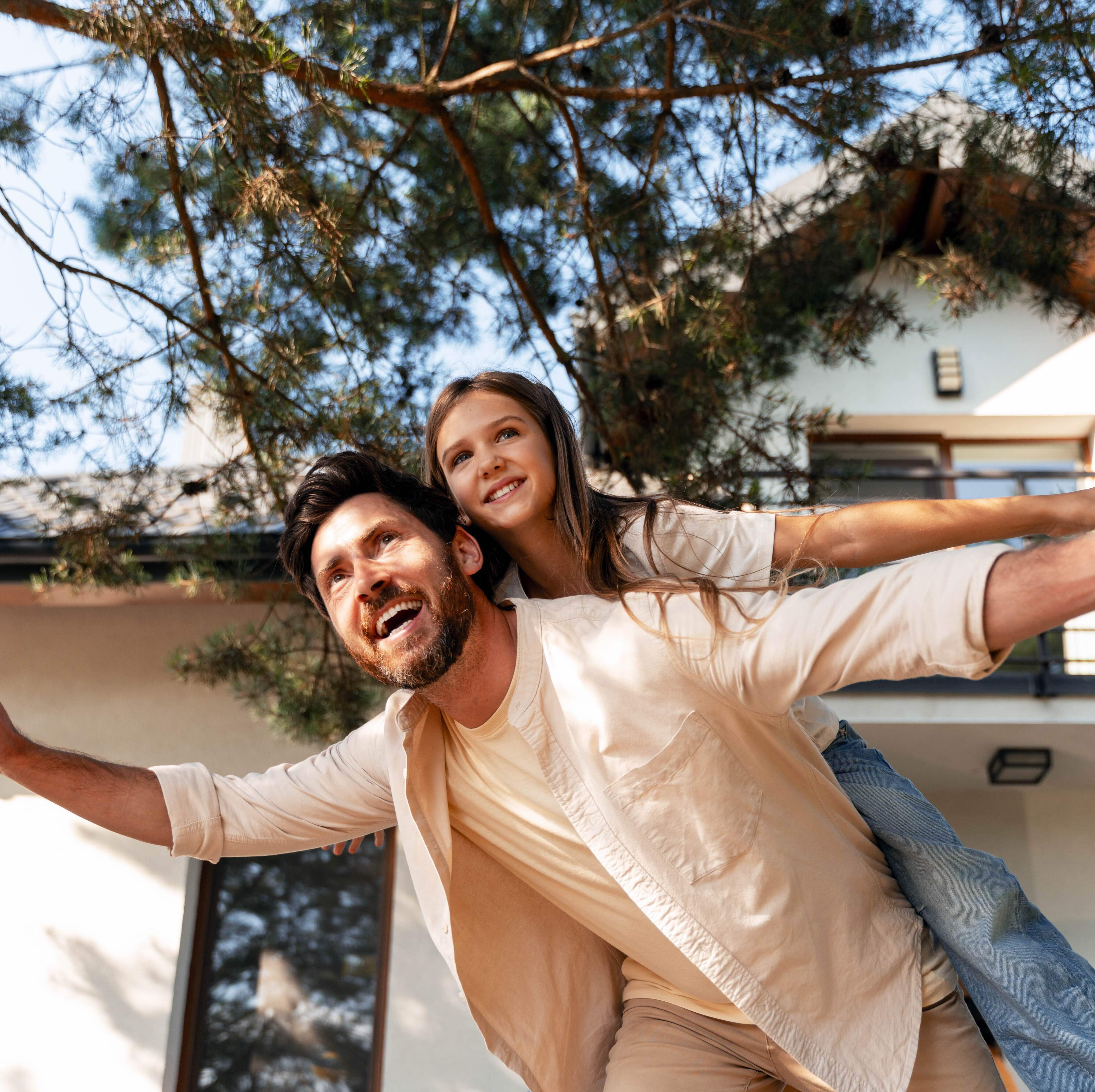 Dad giving daughter piggyback ride outside of new house.