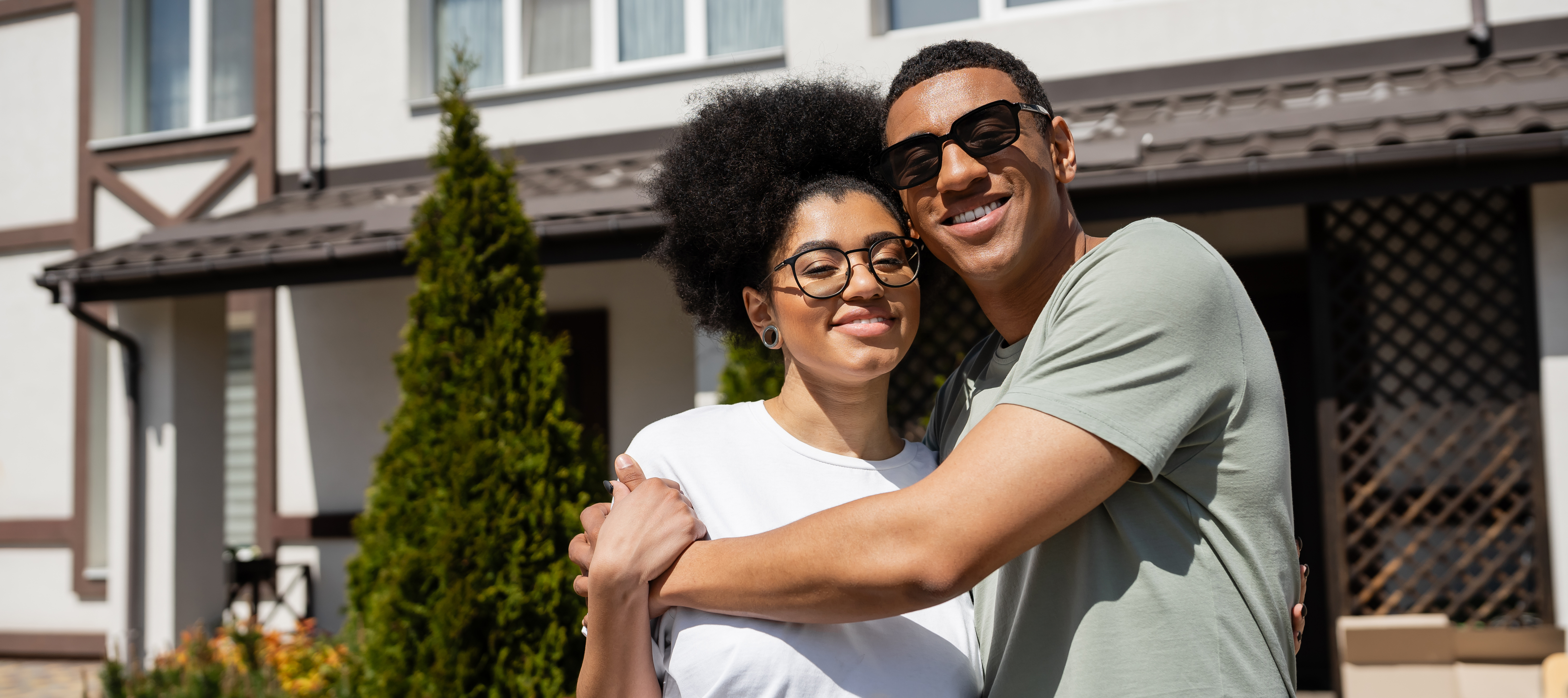 Smiling, happy couple standing outside of home on bright, sunlit day.