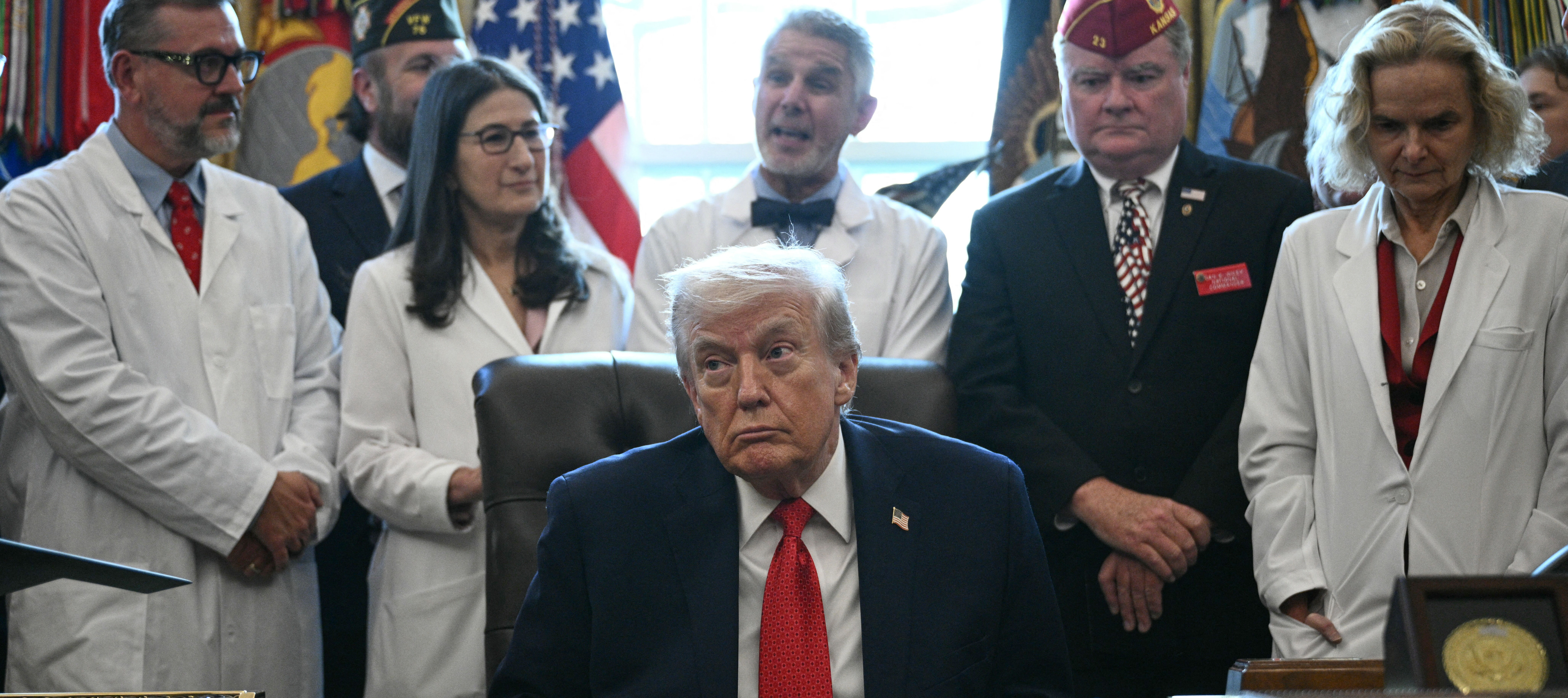 President Trump sits in the oval office with health care professionals behind him.
