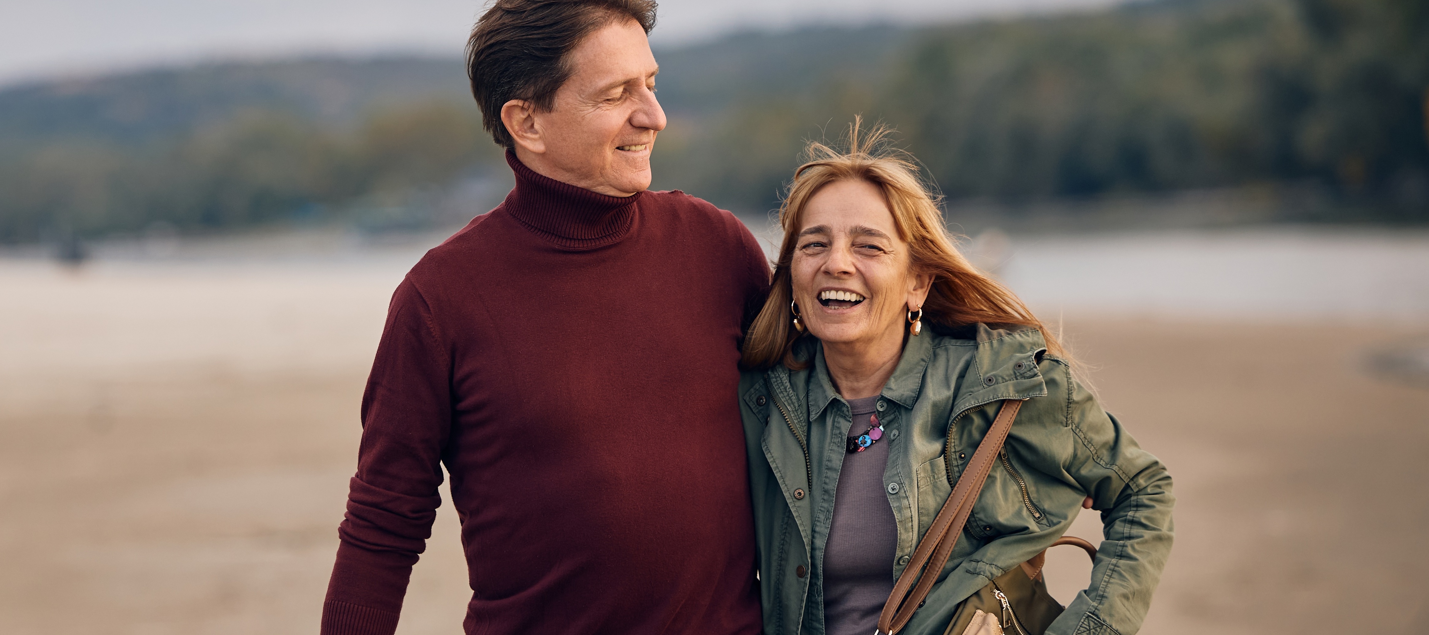 Middle aged couple smiling and walking on a windy beach.
