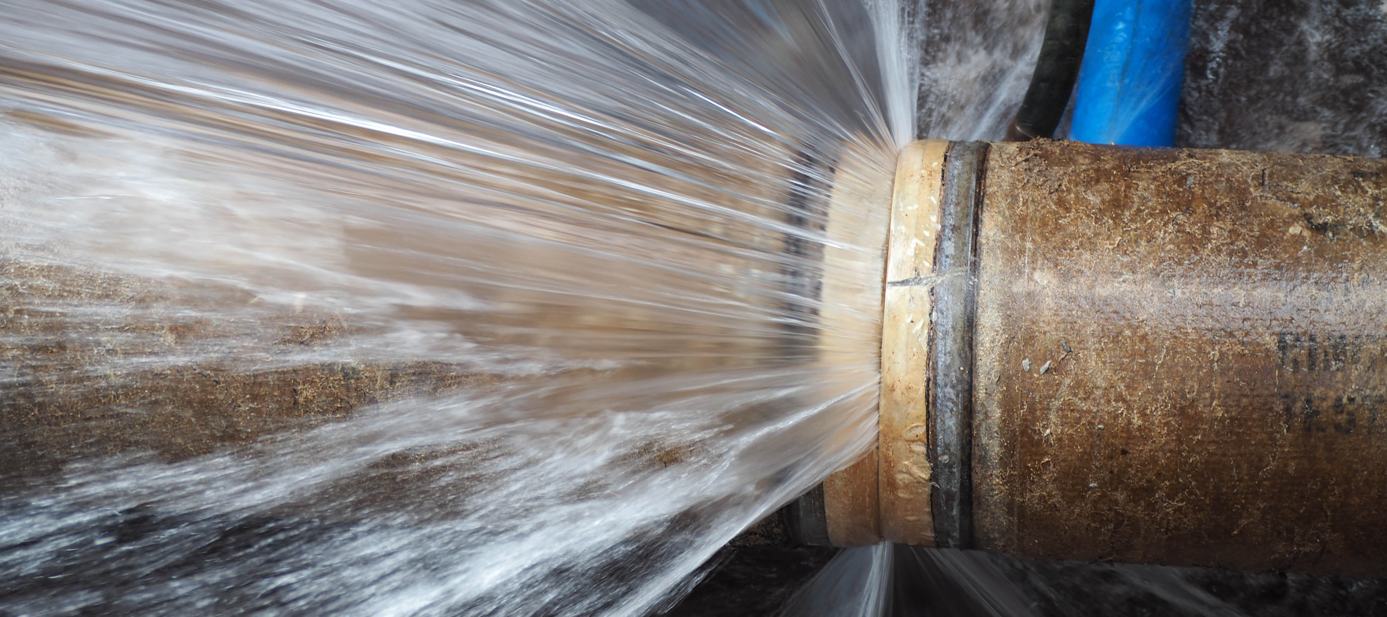 Close up of a pipe that has burst with water spewing out with great force.
