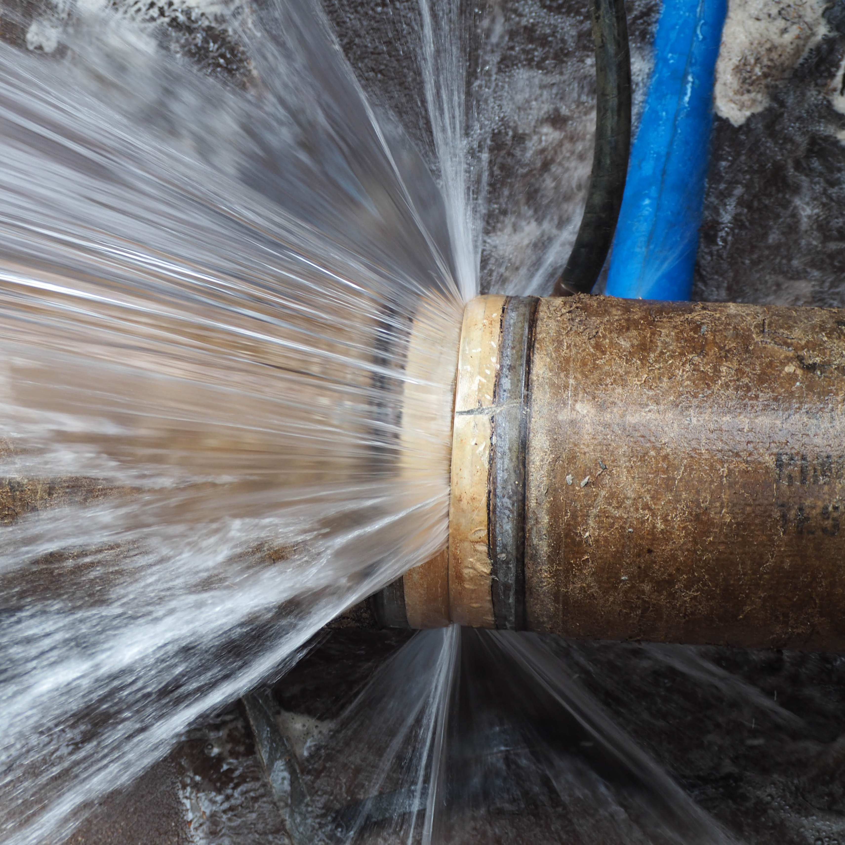 Close up of a pipe that has burst with water spewing out with great force.