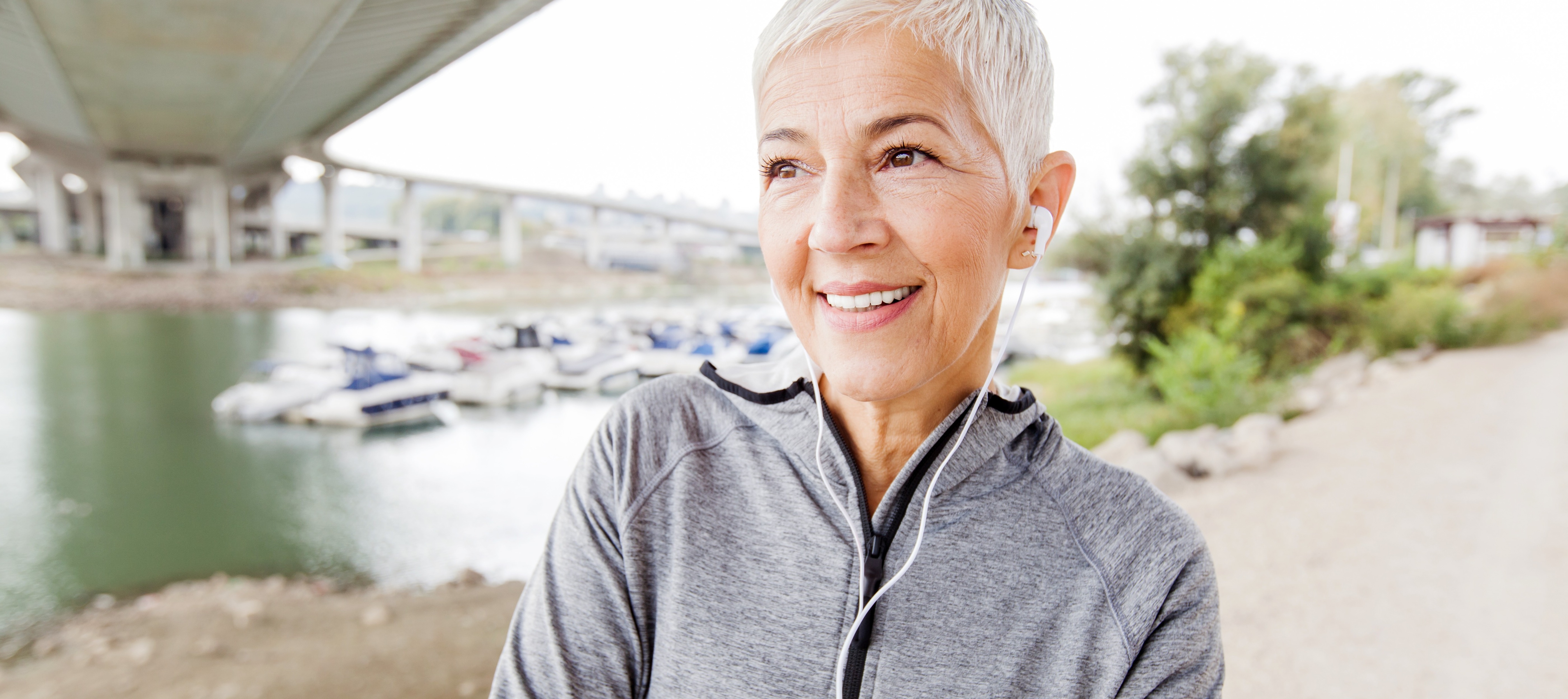 55 year old woman smiling on a walk with headphones in.