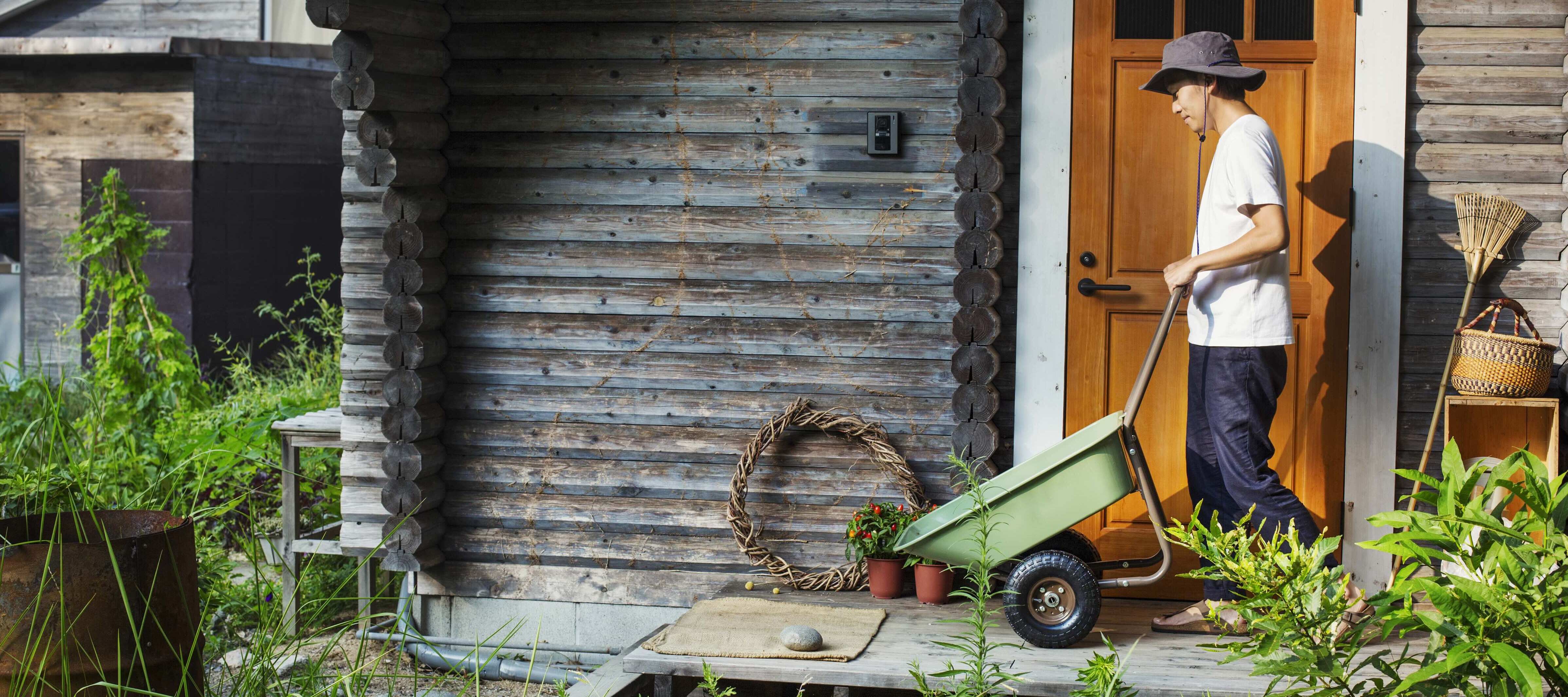 Young woman pushing wheelbarrow outside of childhood home.