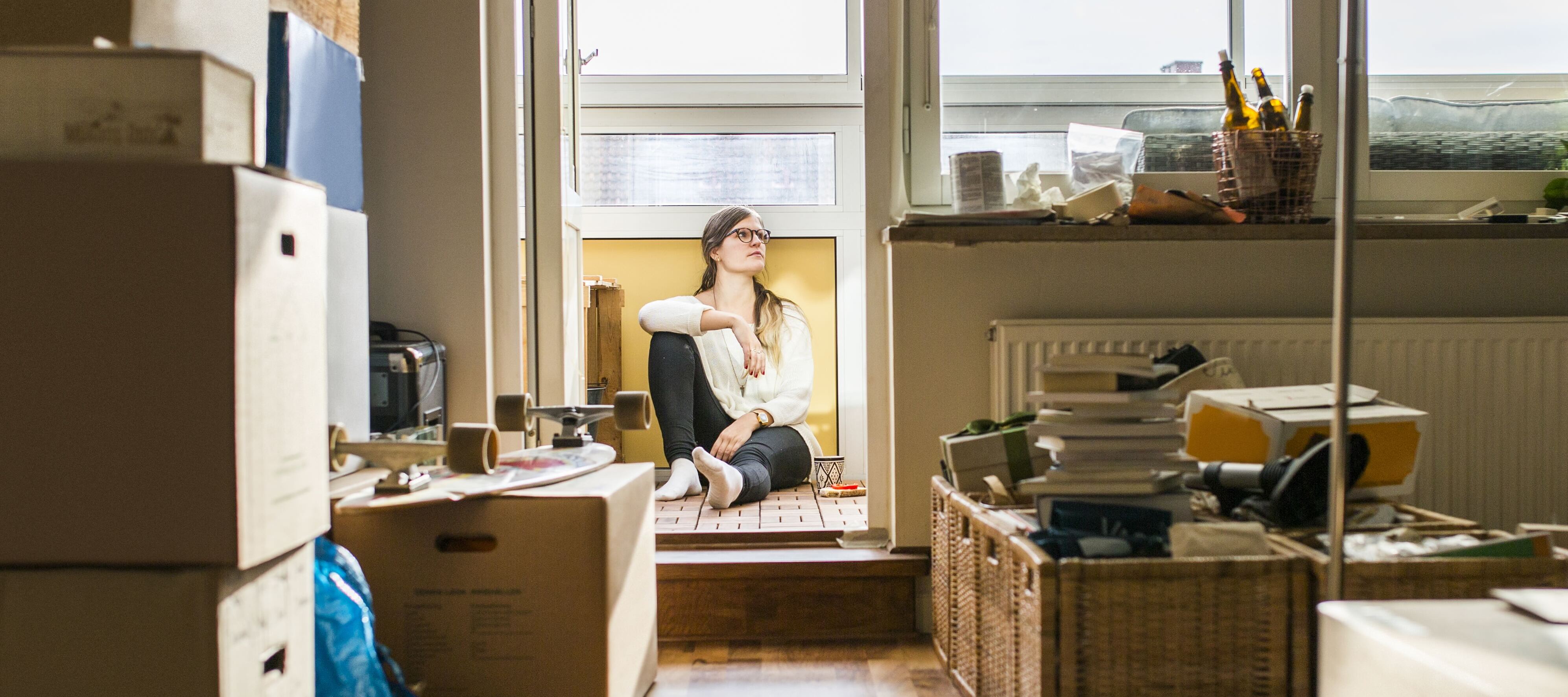 Young woman sitting amongst boxes in her rented apartment.