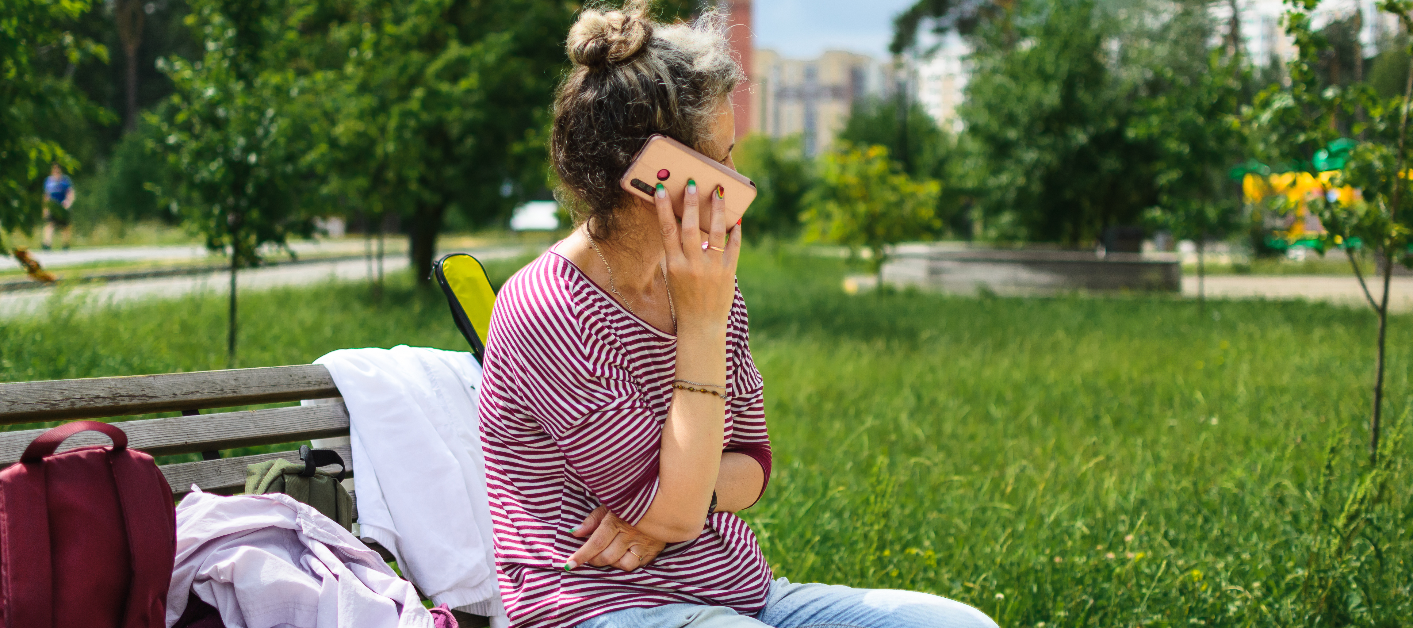A woman answers a phone call while sitting on a park bench.
