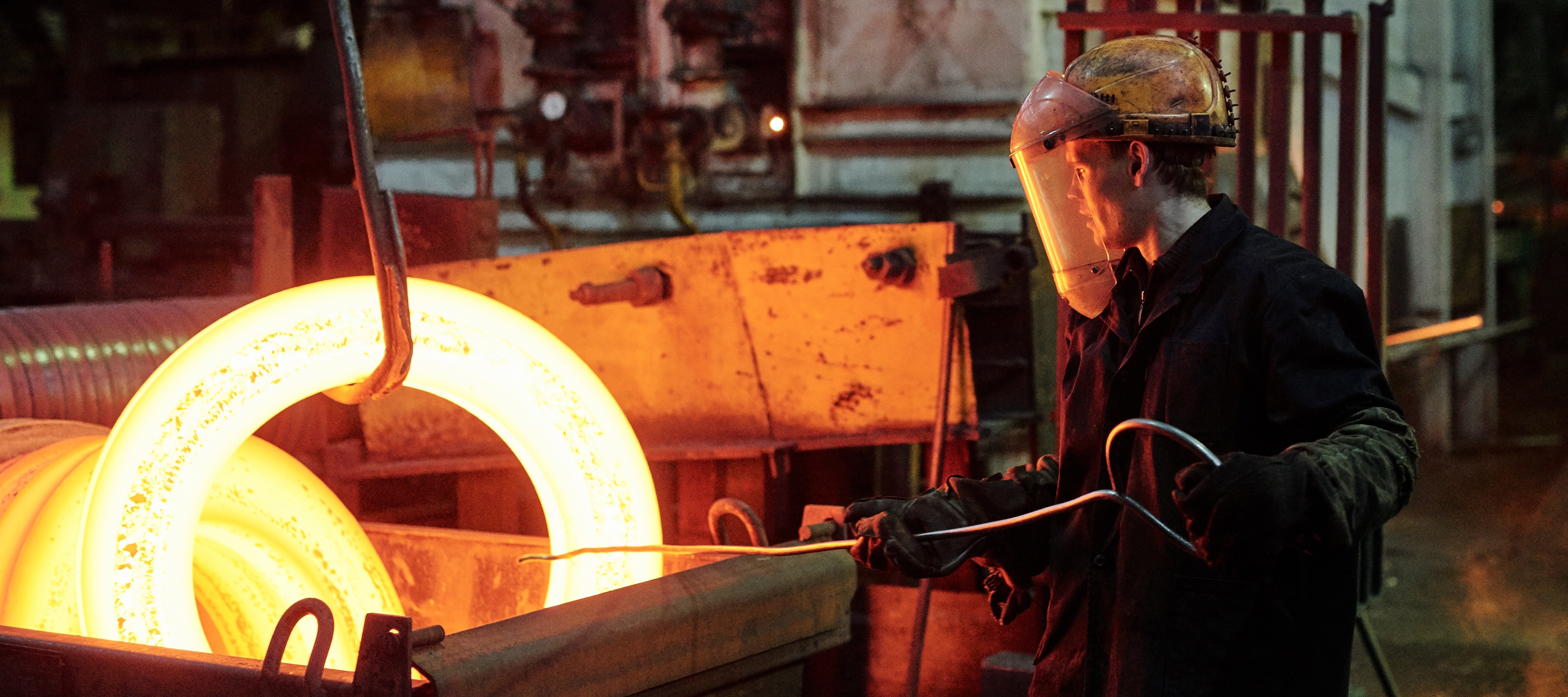 Worker in protective wear melting metal in a factory.