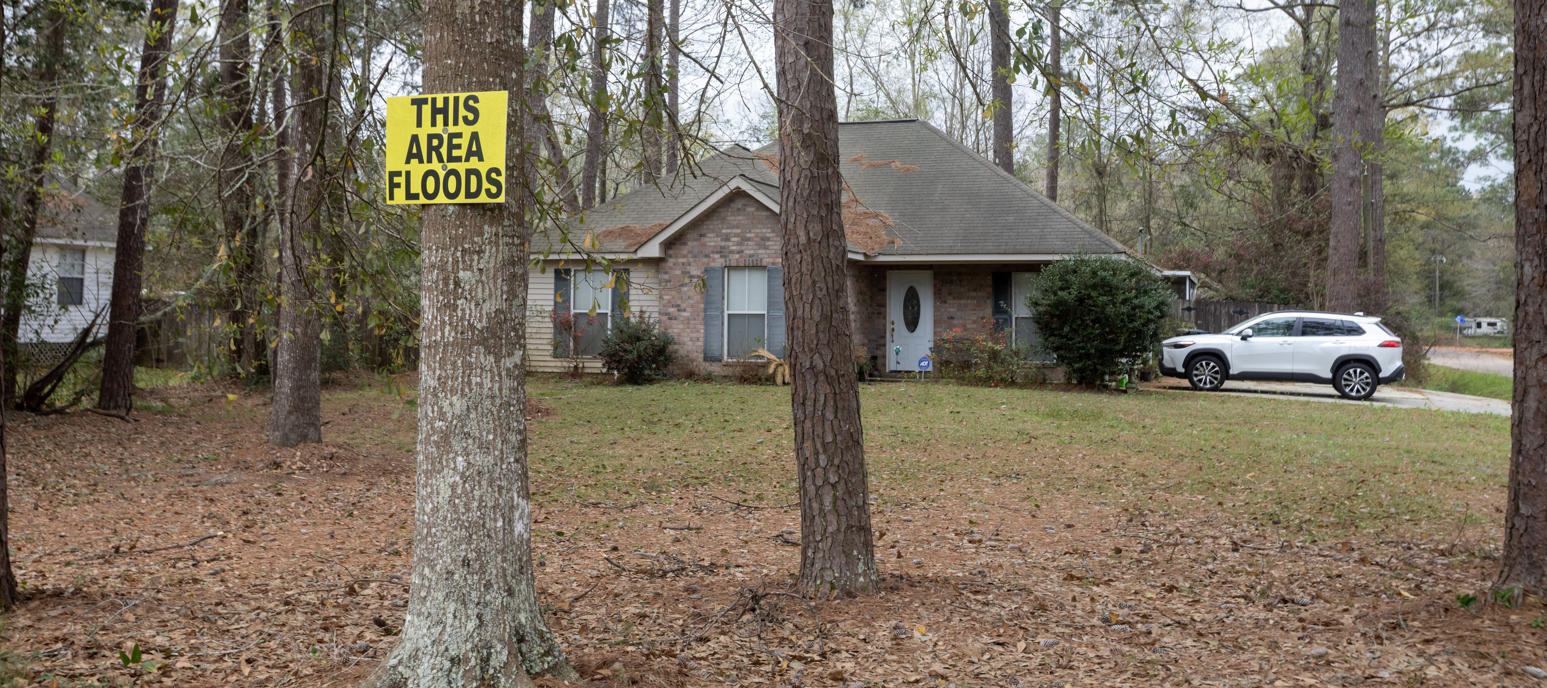 A flood warning sign is placed on a tree near a house.