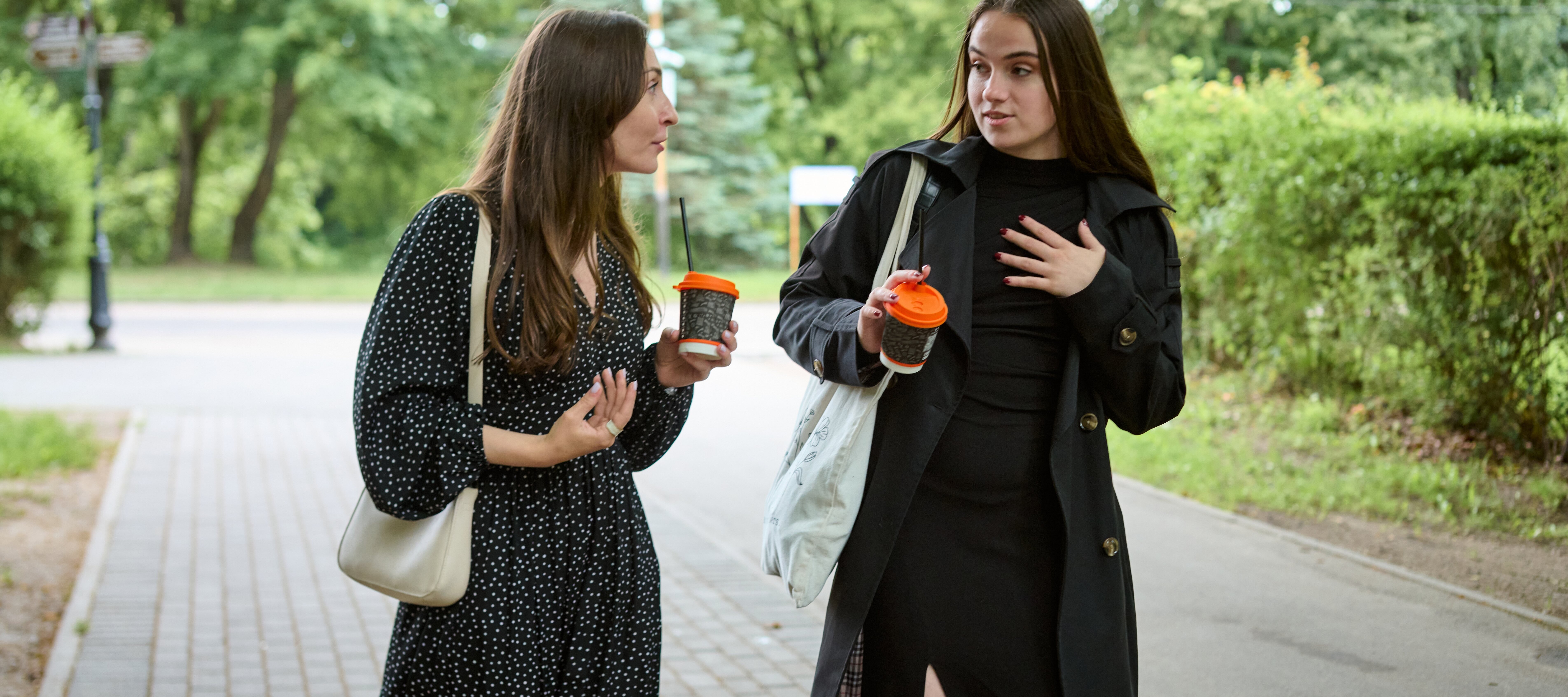 Two young women chatting and walking with coffee in their hands.