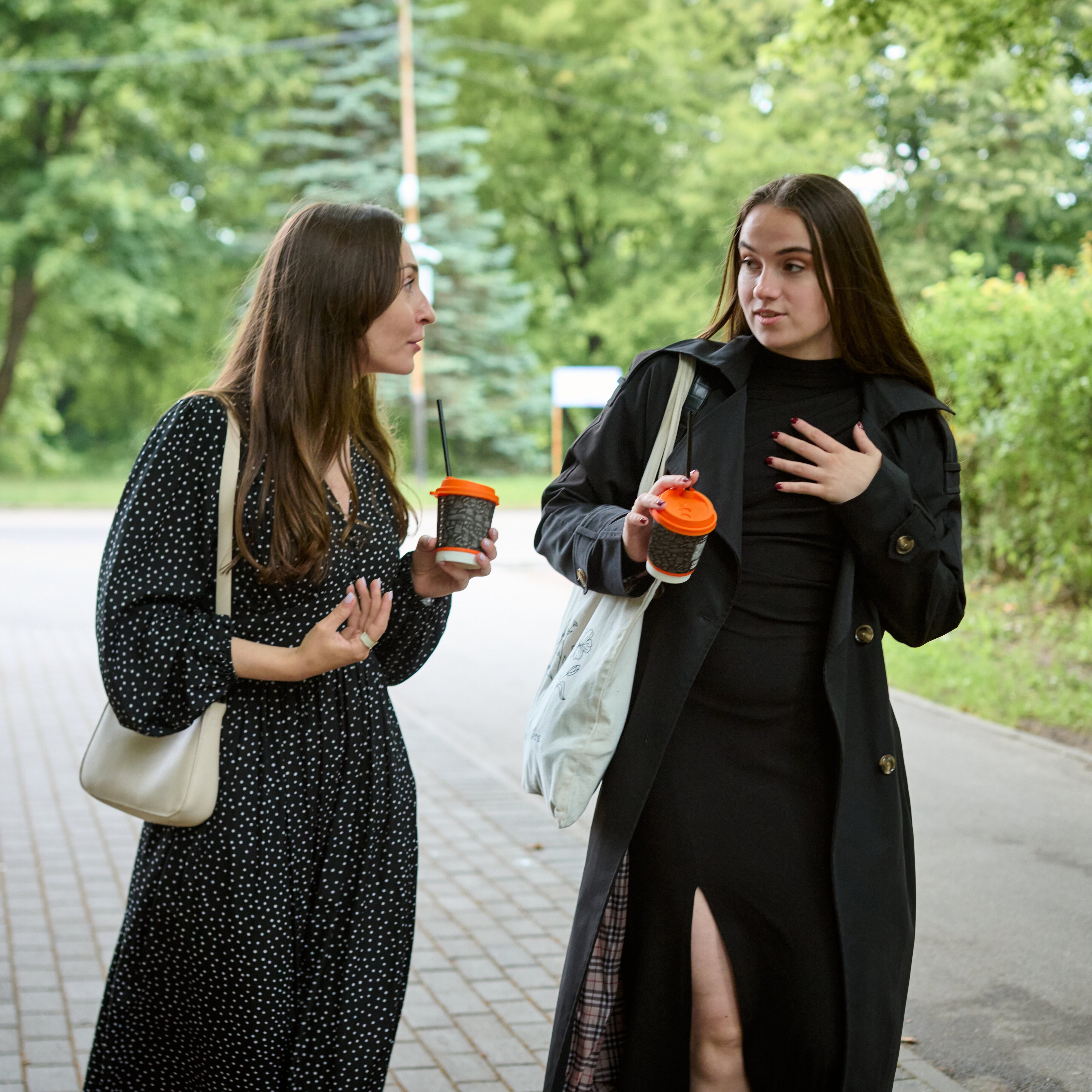 Two young women chatting and walking with coffee in their hands.