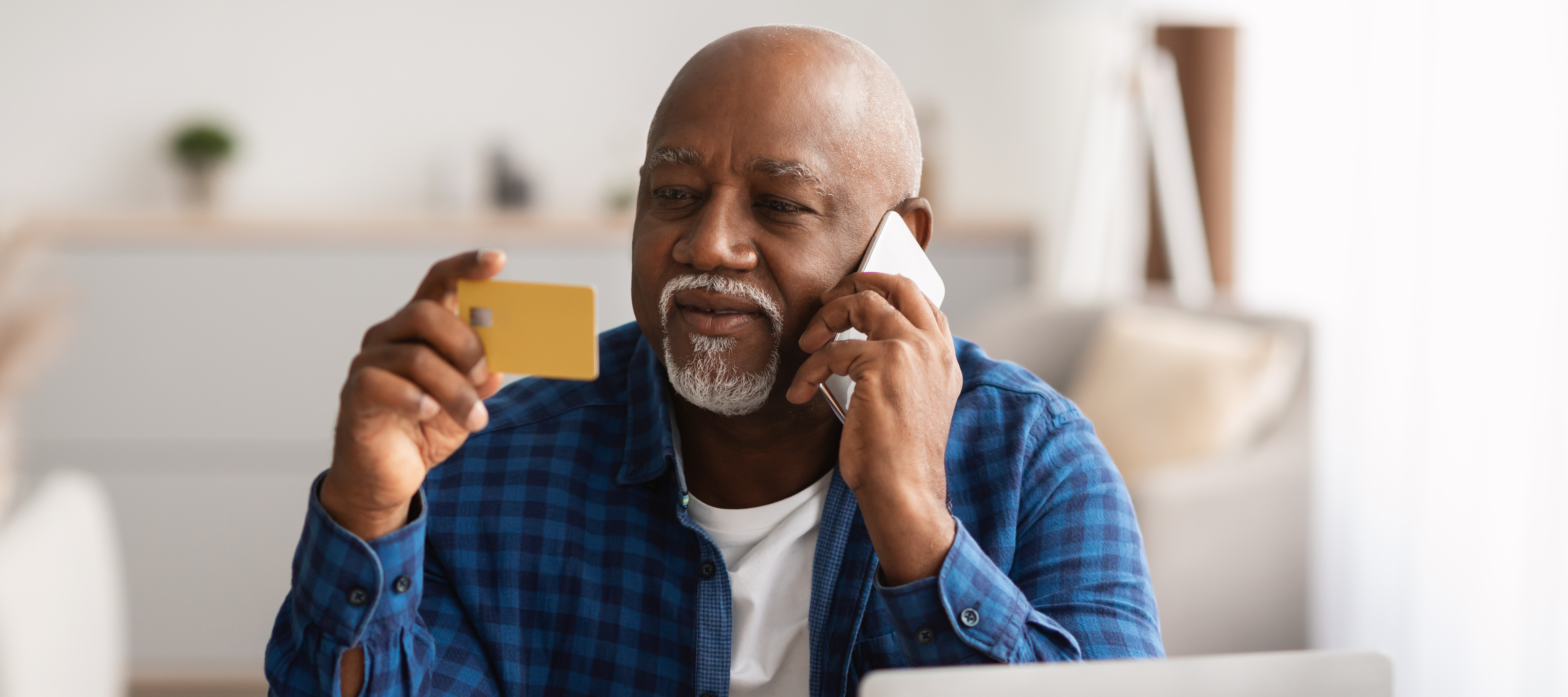Man sitting at desk while on the phone, holding a credit card in one hand and looking at the back of it.