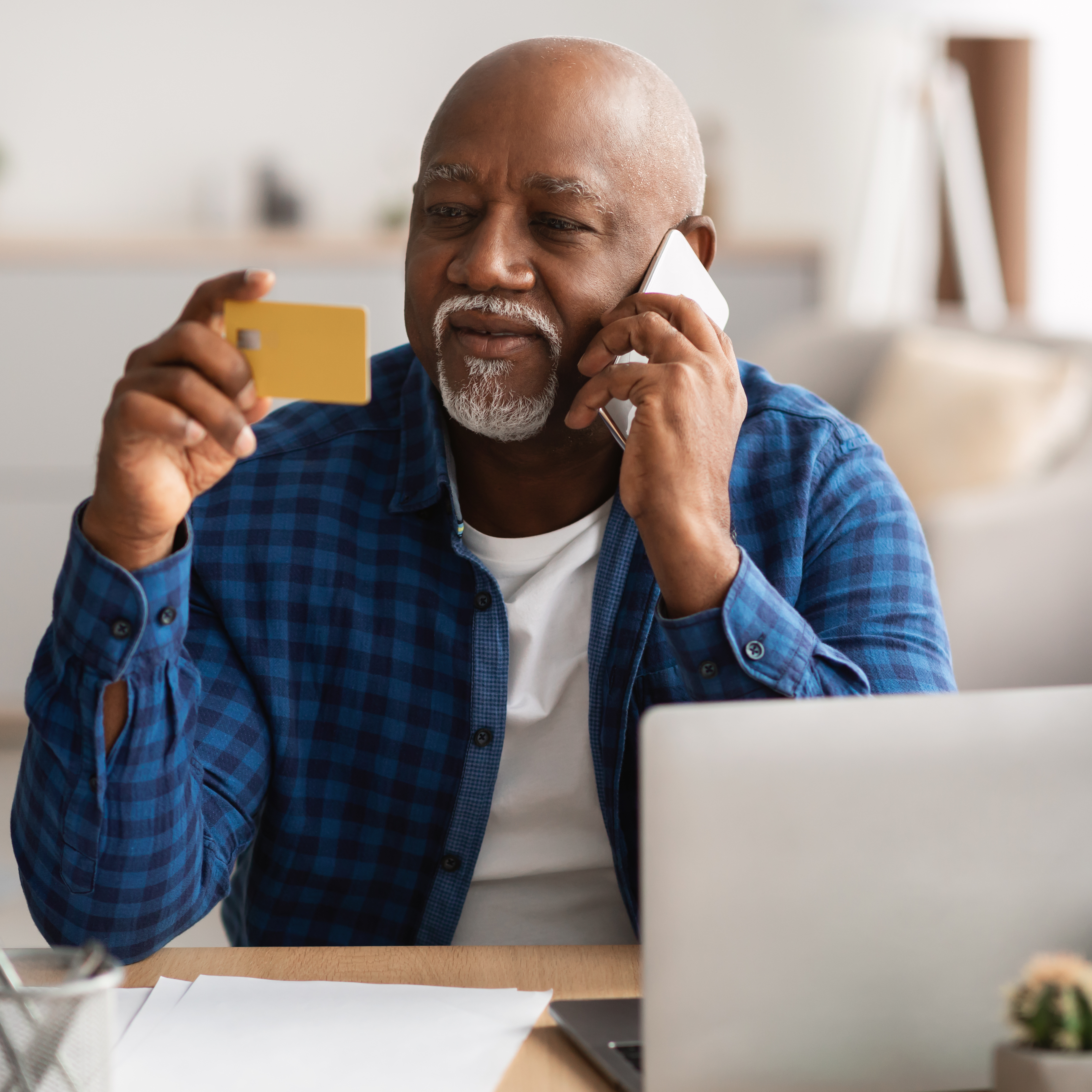 Man sitting at desk while on the phone, holding a credit card in one hand and looking at the back of it.
