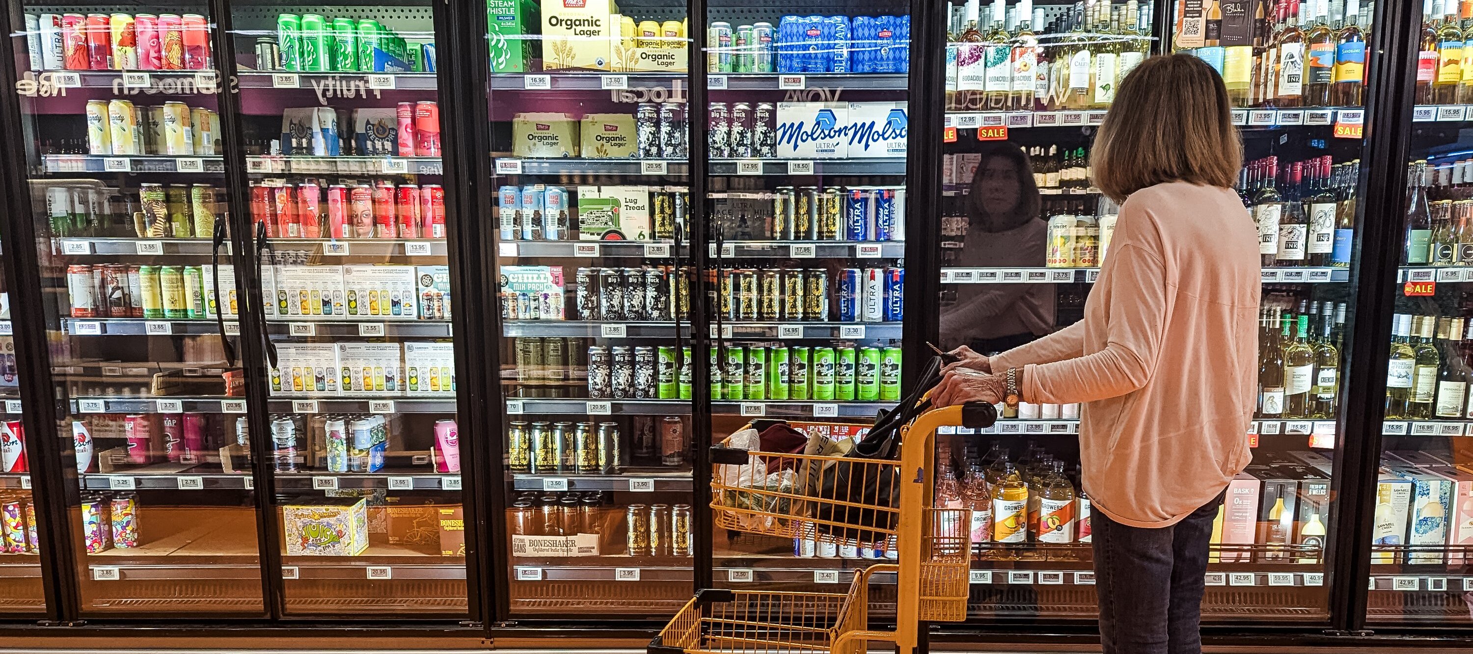 Woman in a grocery store with a shopping cart looking at items through a display case.