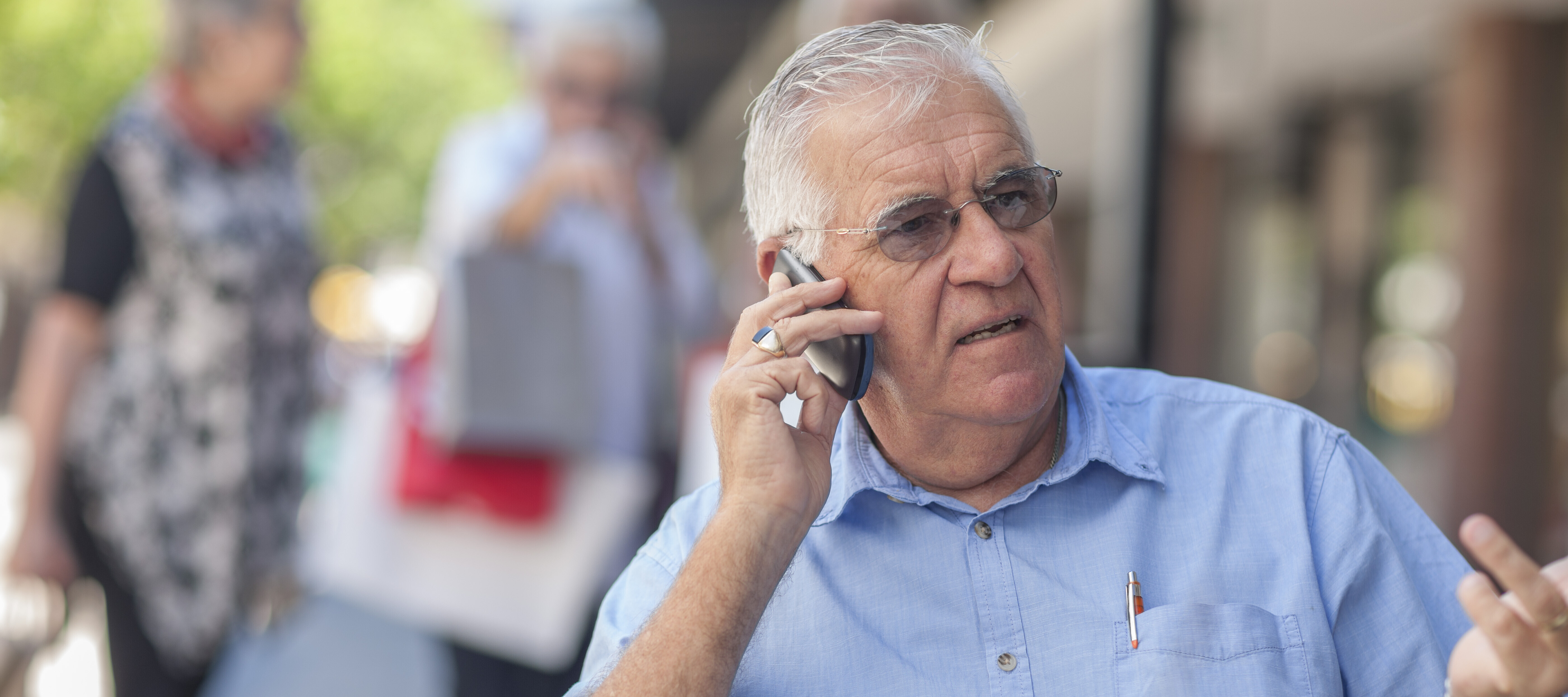 Senior man sitting outside at a cafe, talking on the phone, looking concerned.