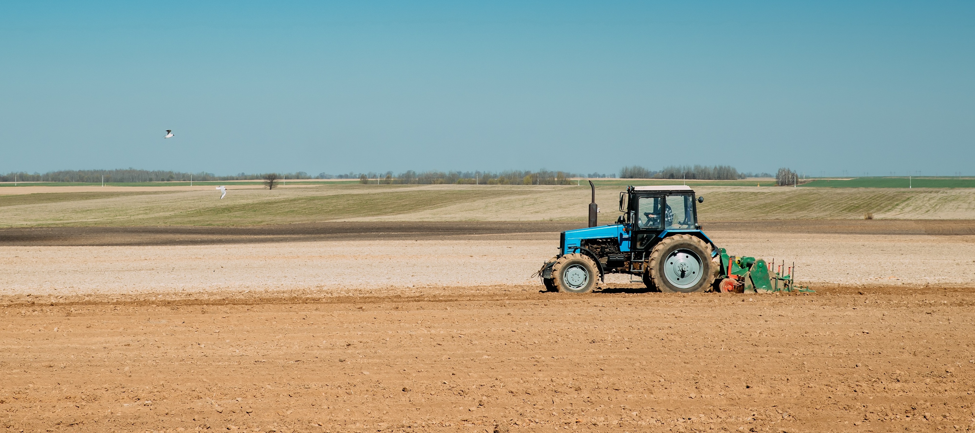 Wide angle shot of a lone tractor plowing a barren field of land.