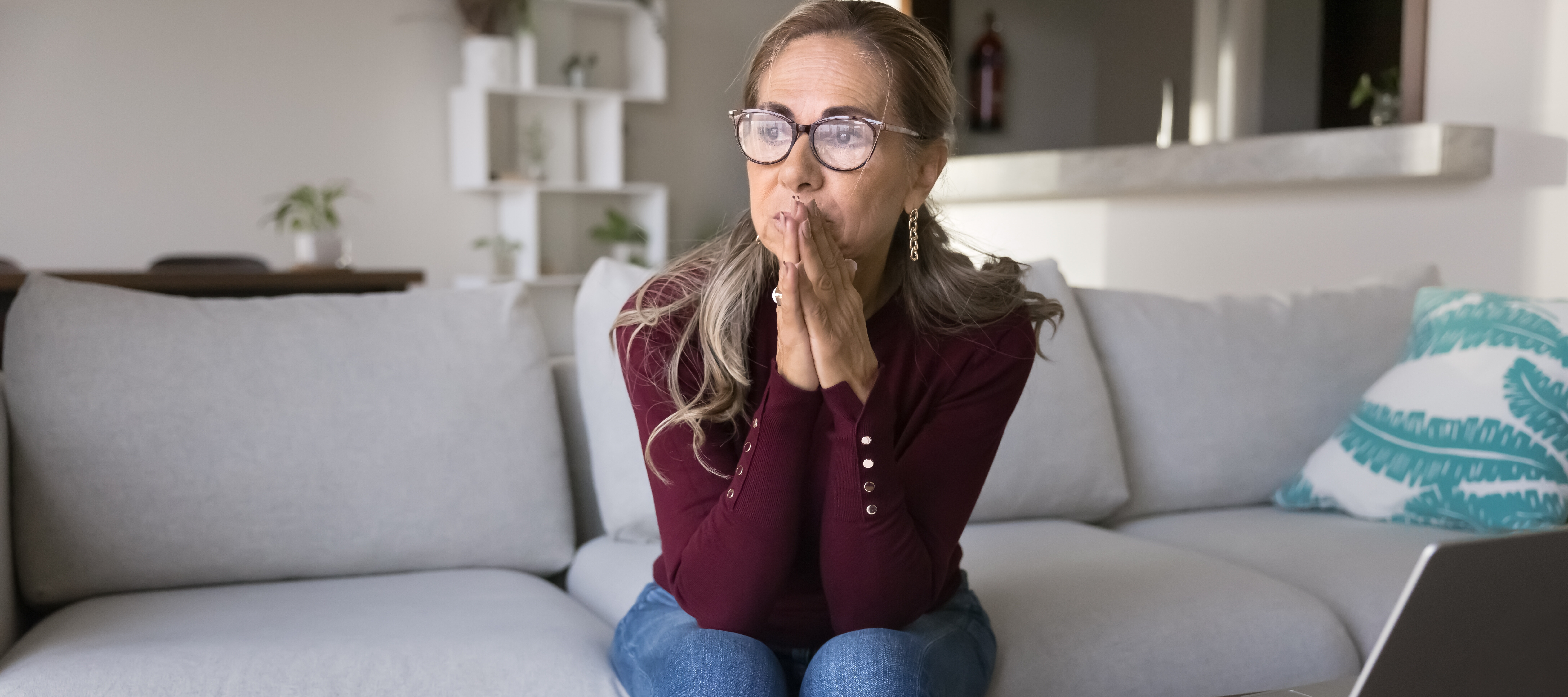 A concerned woman sits pensively in her living room.