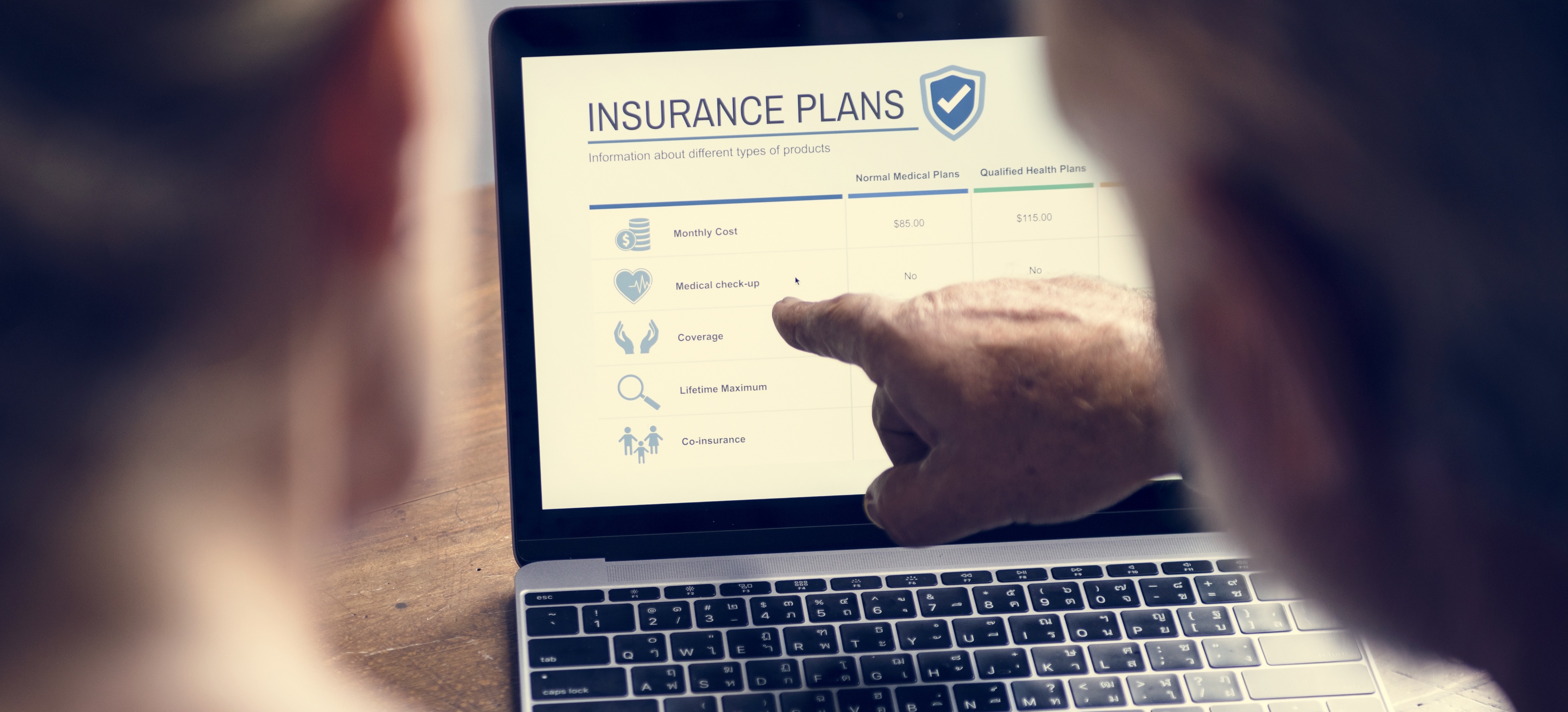 View from behind of two people on a computer, one pointing at the screen that says "Insurance Plans."