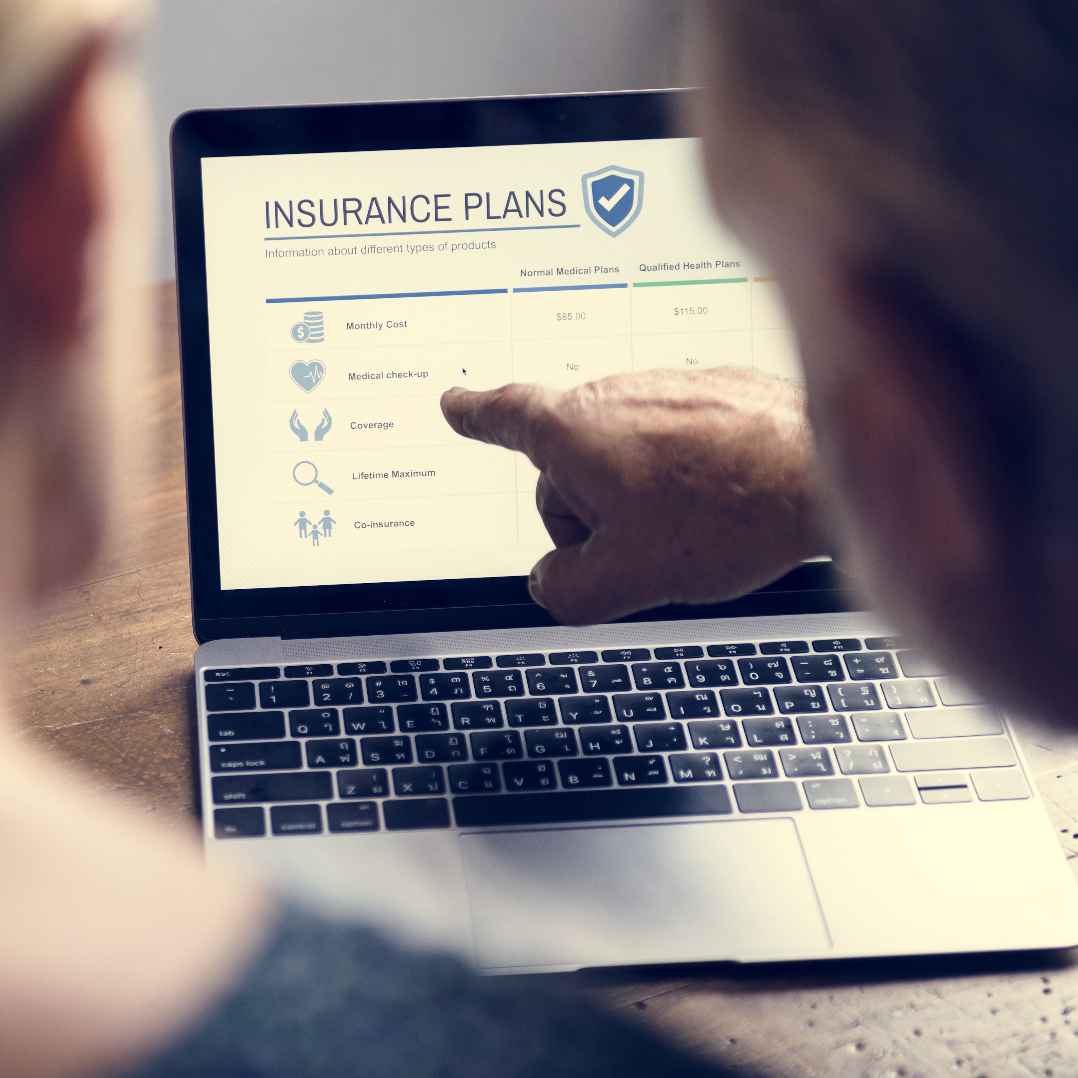 View from behind of two people on a computer, one pointing at the screen that says "Insurance Plans."