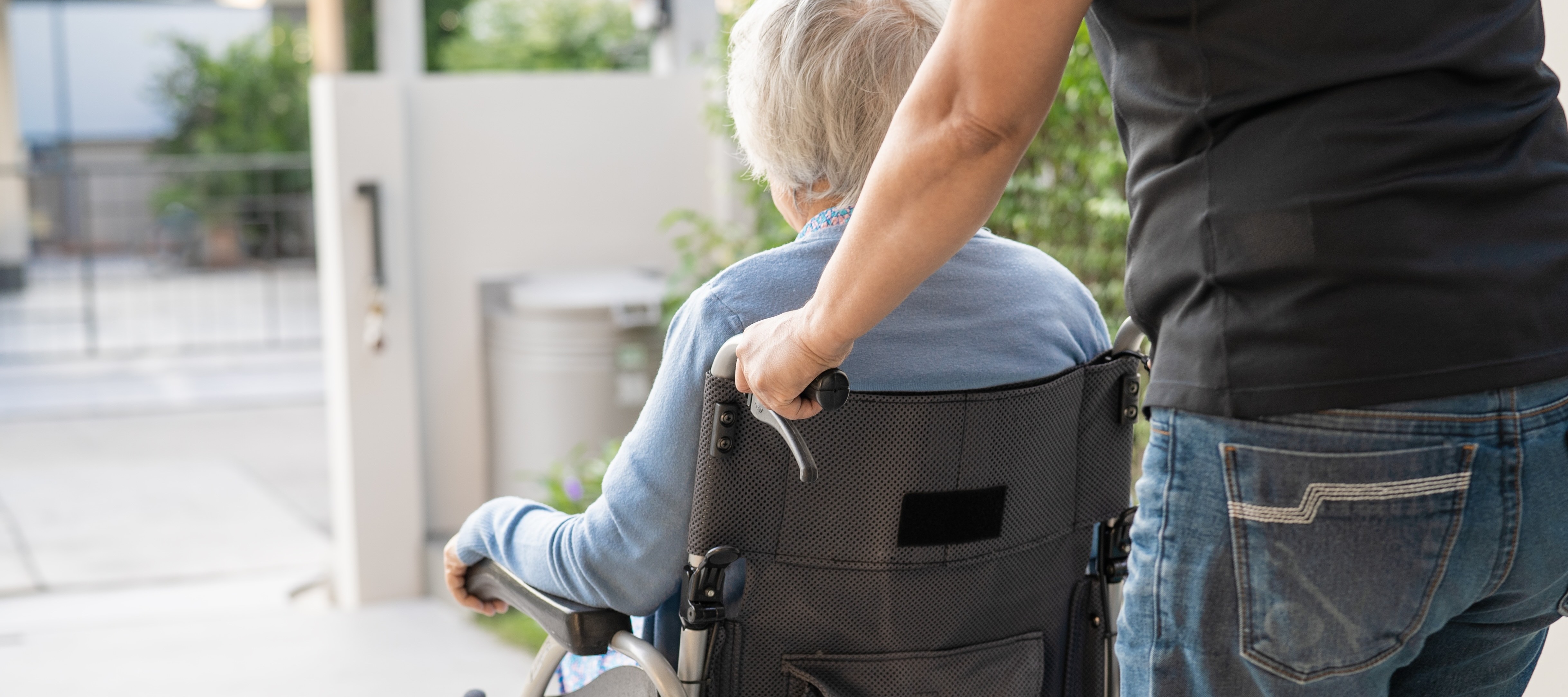 Caregiver pushing elderly woman in a wheelchair.