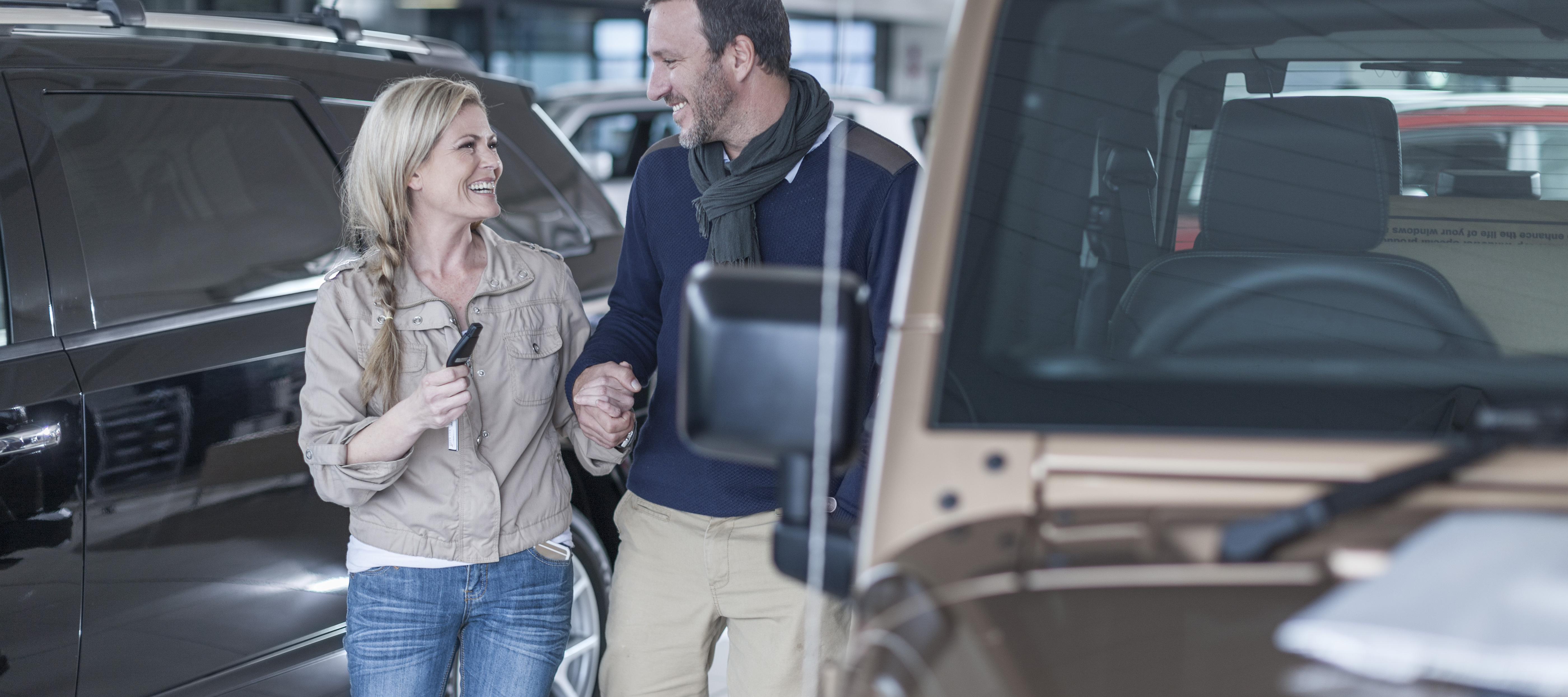 Middle-aged couple smiling next to new car at dealership.