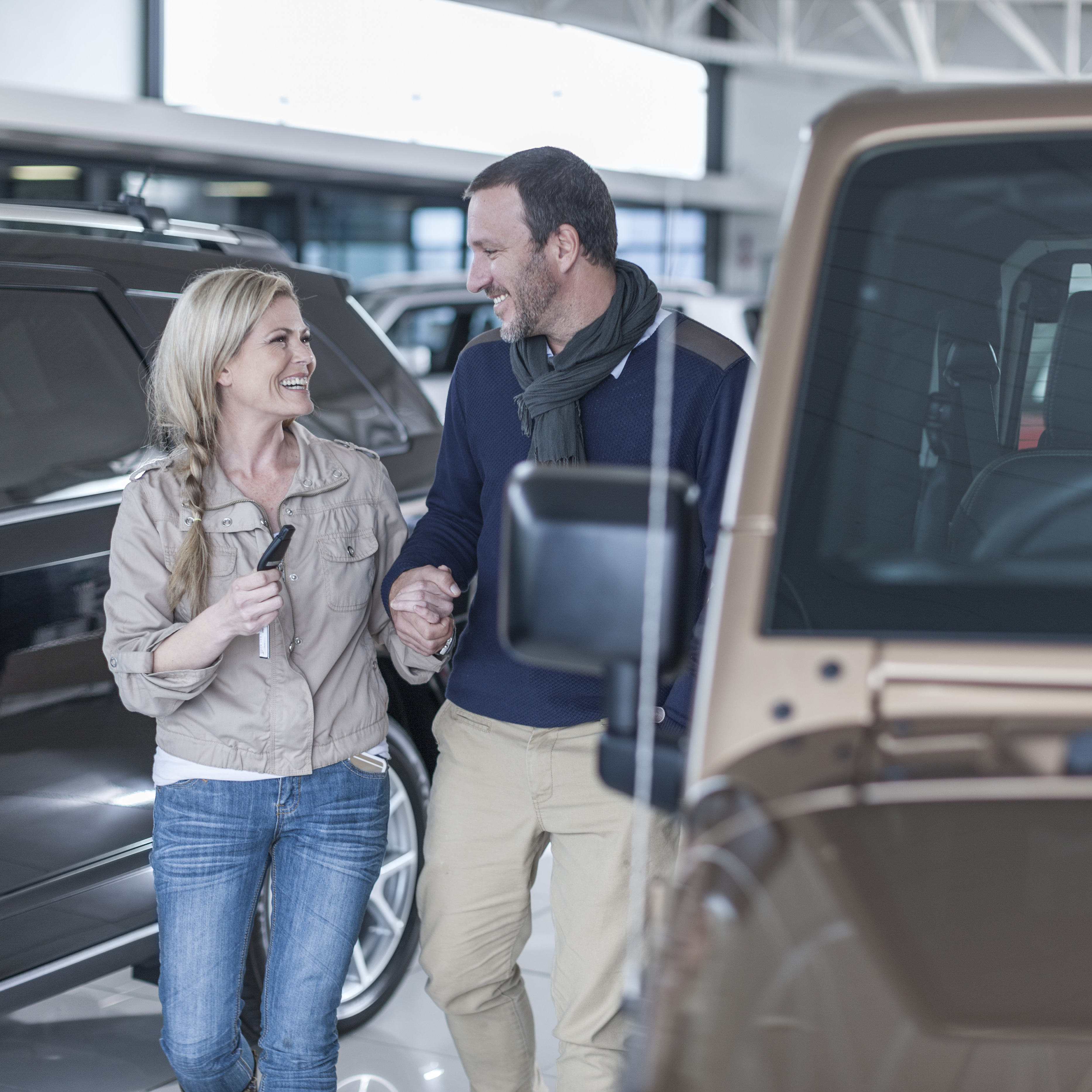Middle-aged couple smiling next to new car at dealership.