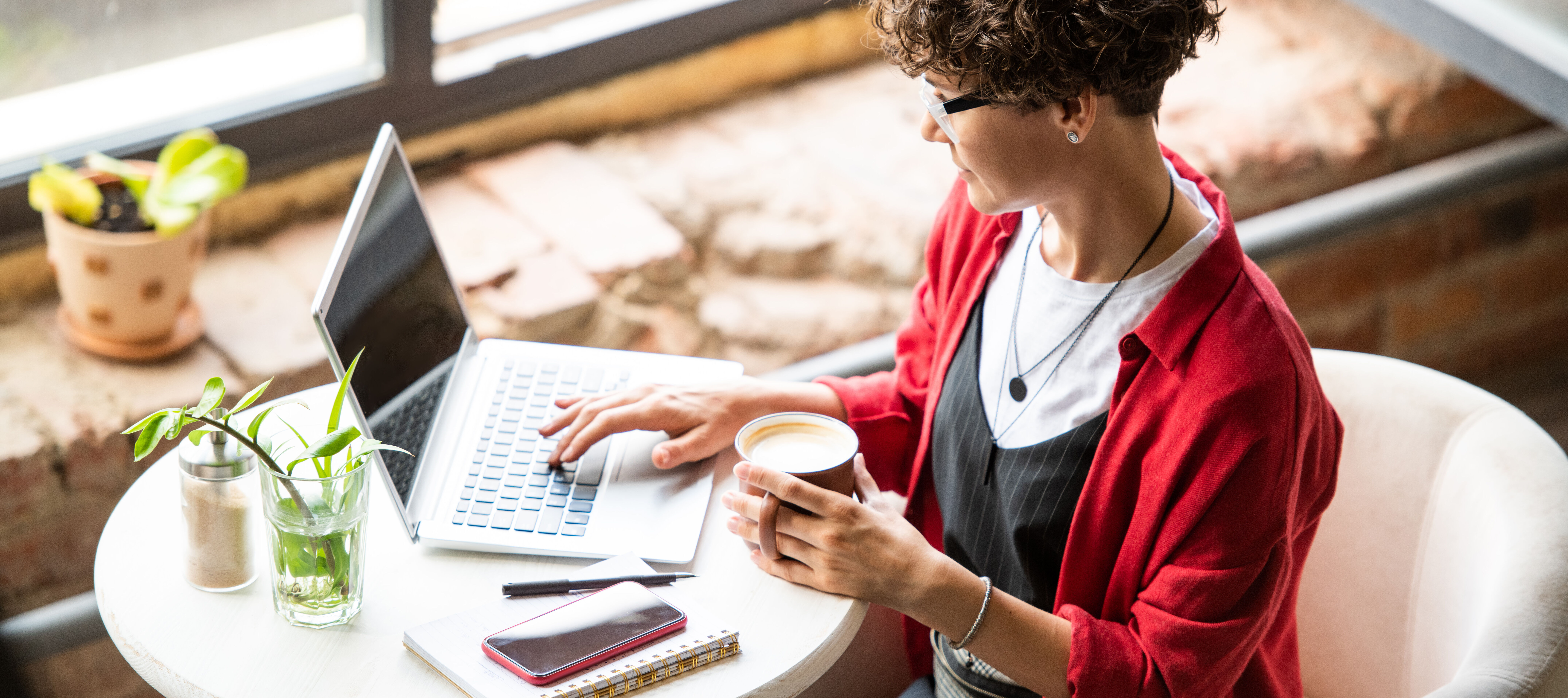 A woman looks at her computer while sipping coffee.
