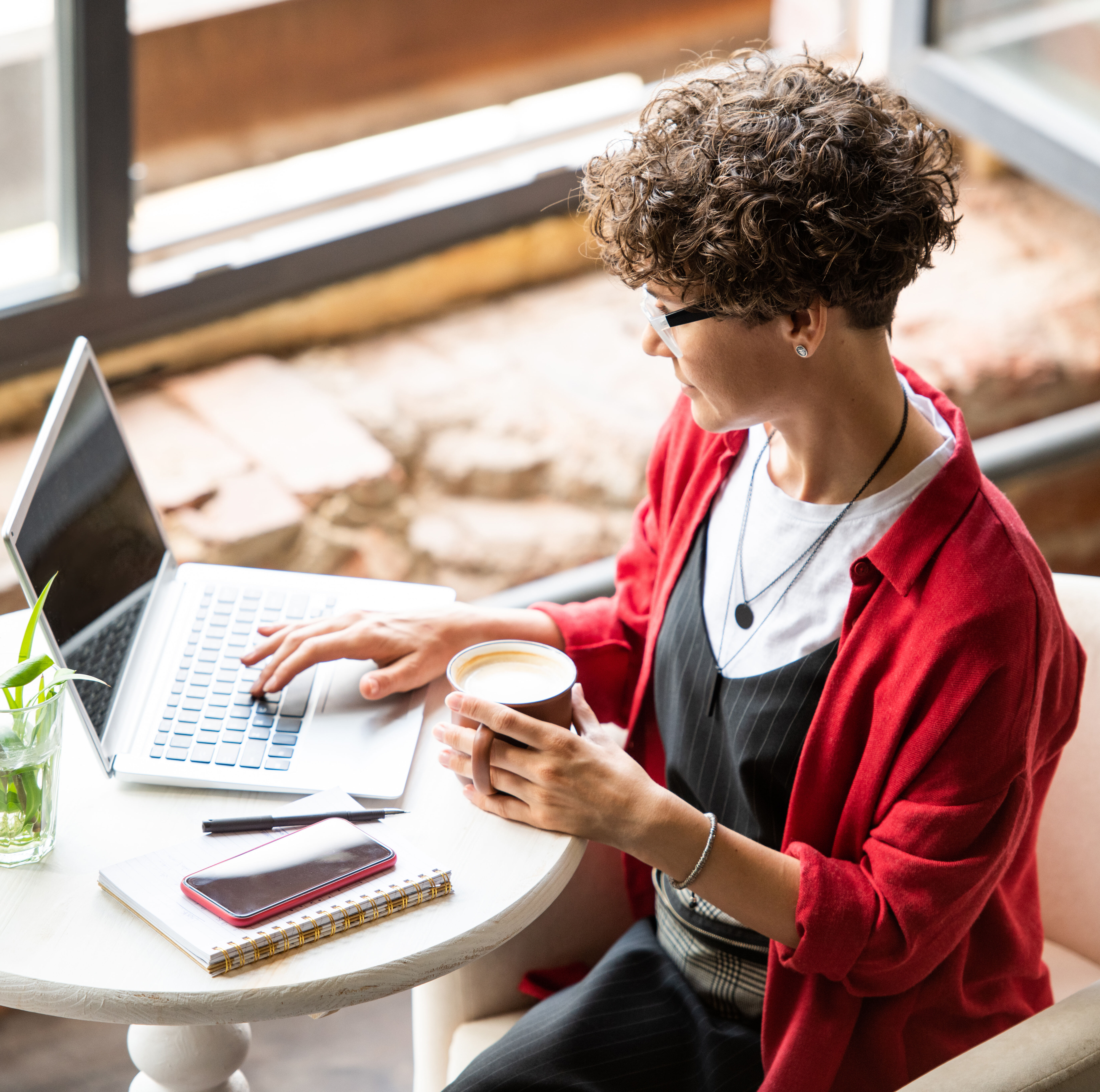 A woman looks at her computer while sipping coffee.