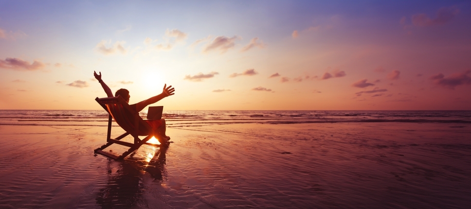 Happy freelancer with laptop computer working on the beach.