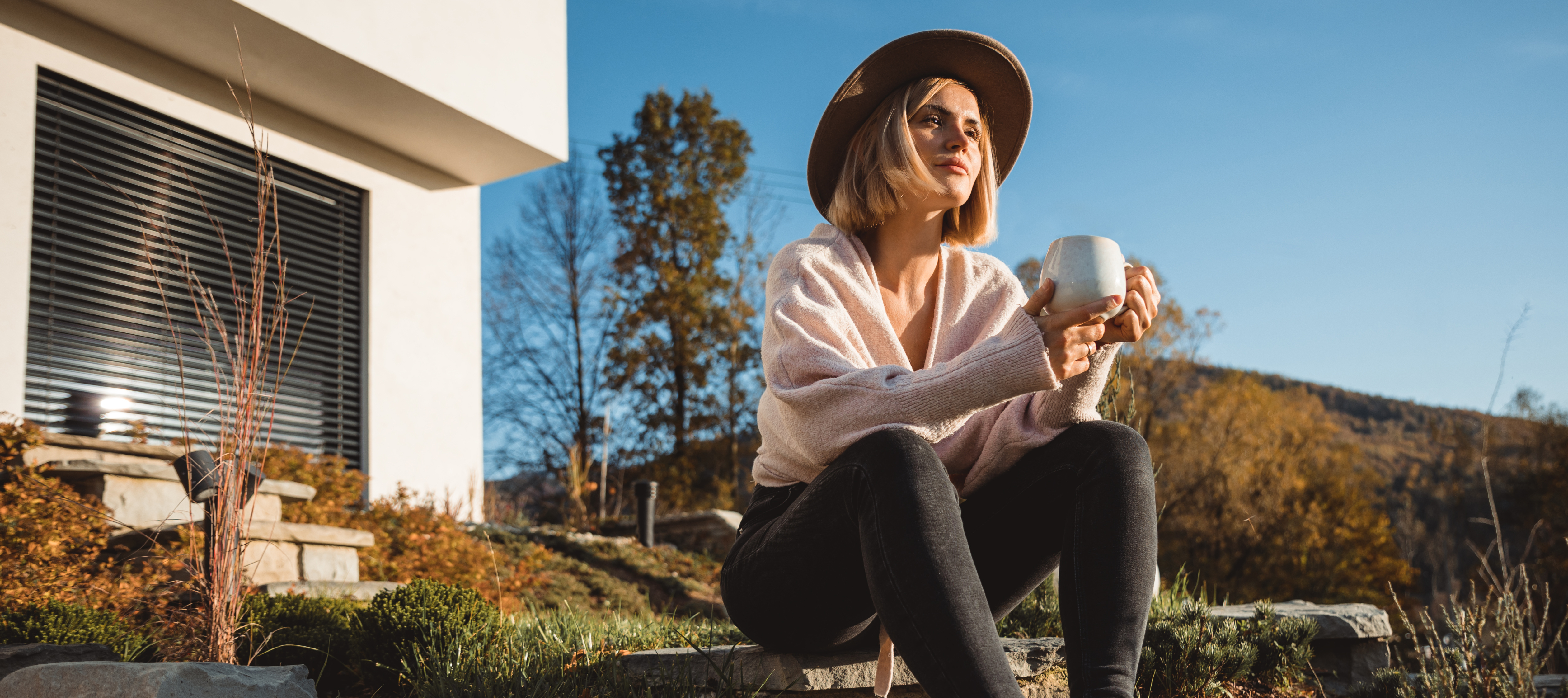 A woman sits on the steps in front of her home drinking a cup of coffee.