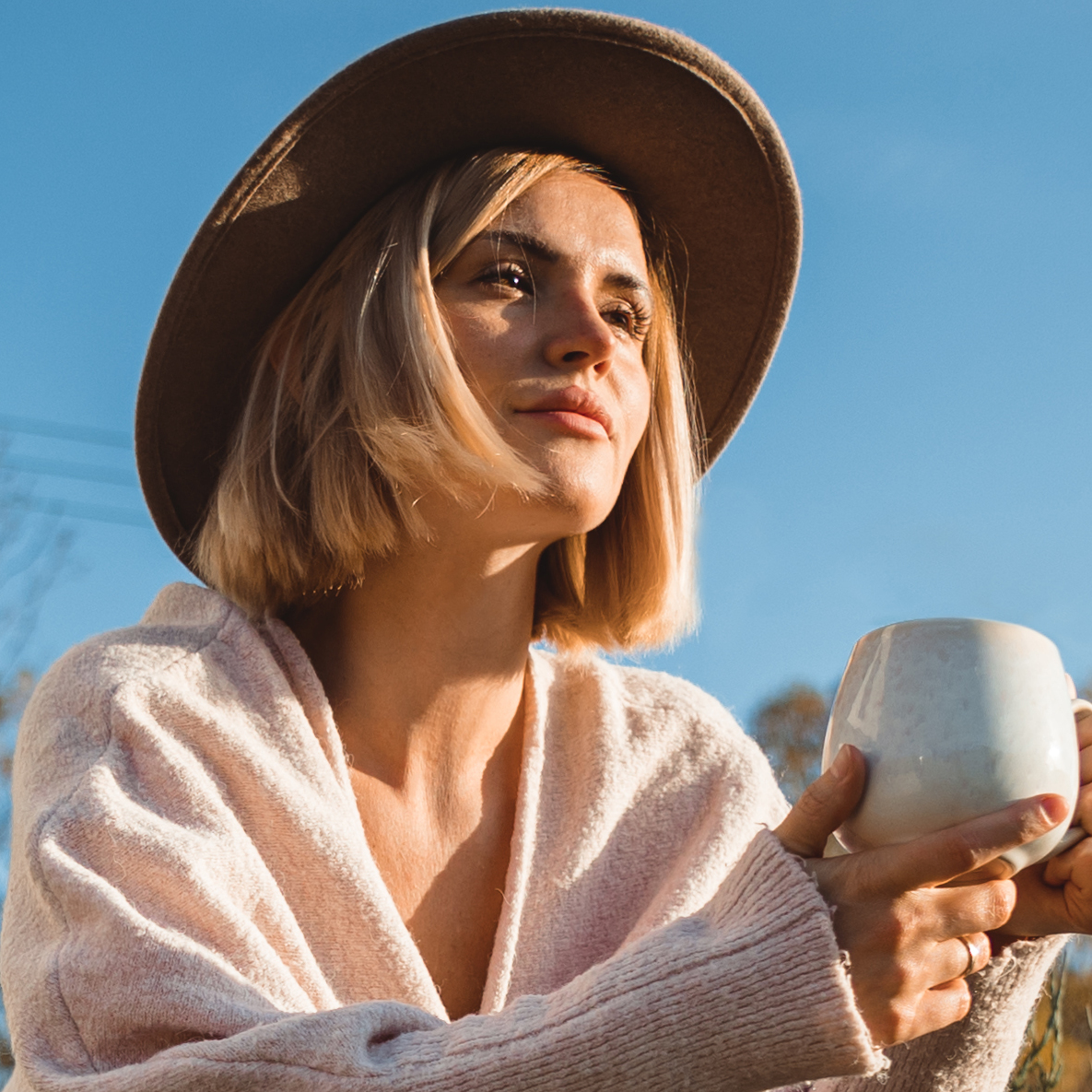 A woman sits on the steps in front of her home drinking a cup of coffee.