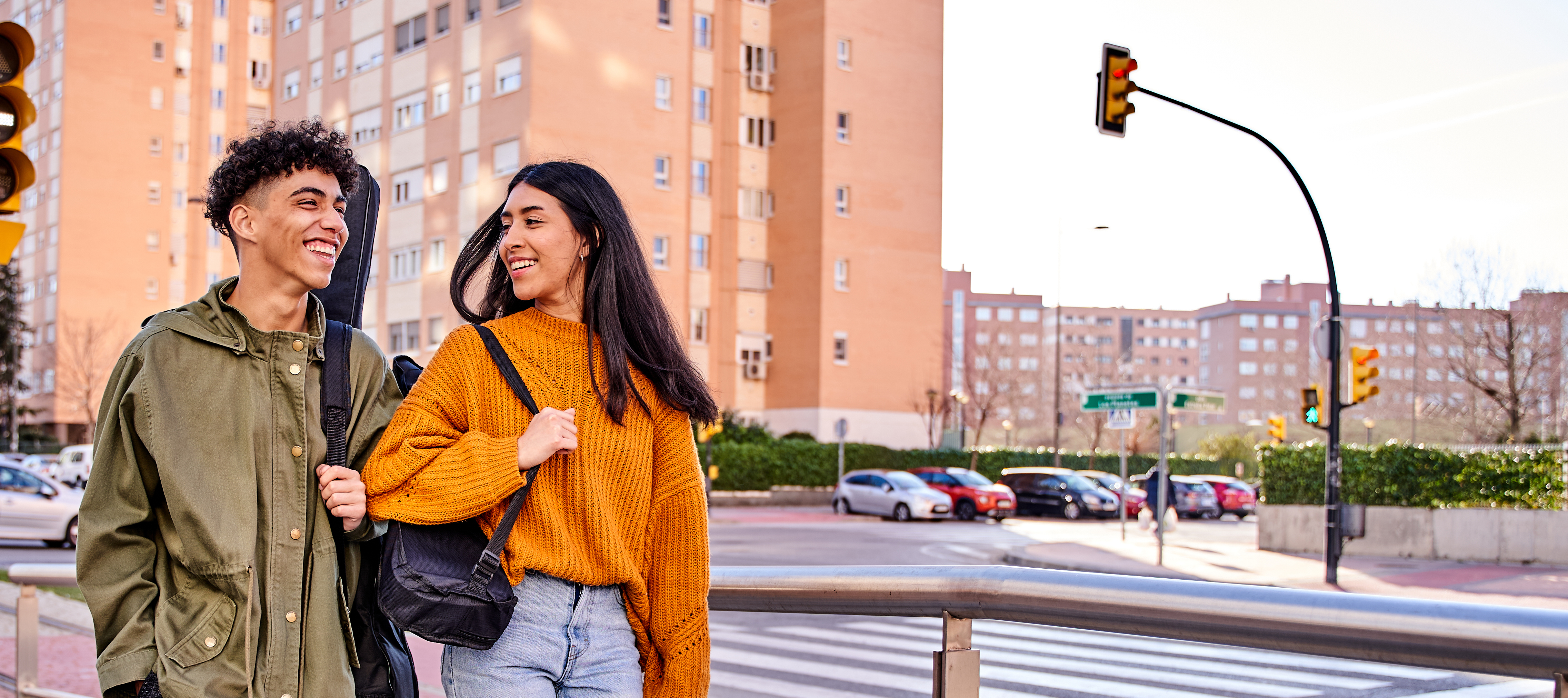 A pair of friends walking in a city environment with high rise buildings behind them, looking happy.