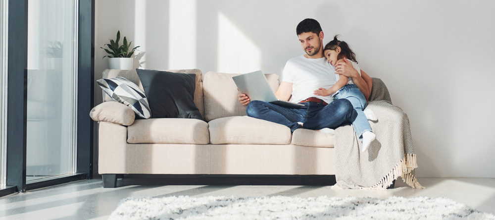 Stay-at-home dad sitting with his daughter, looking at a laptop, spending free time at home together.