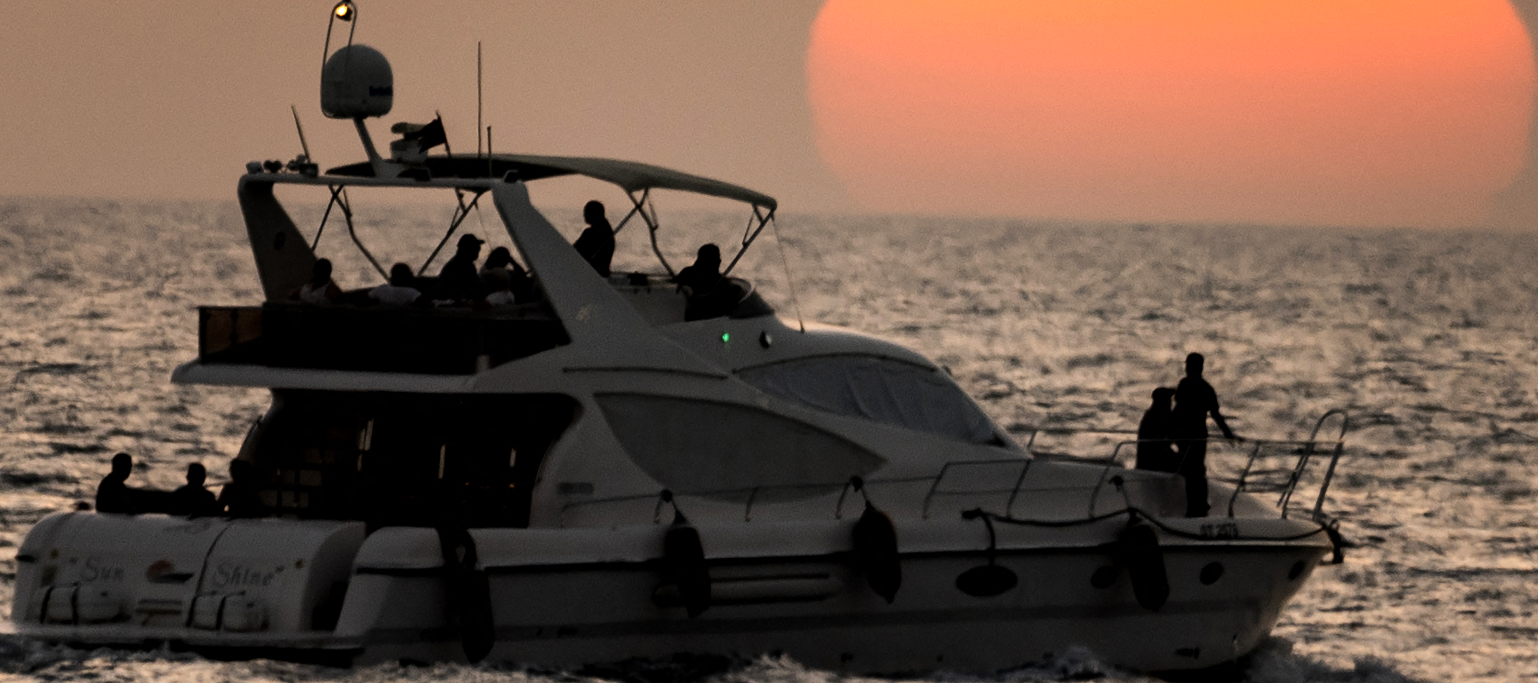 People on a yacht are sihouetted against the setting sun in Dubai, June 11, 2025.