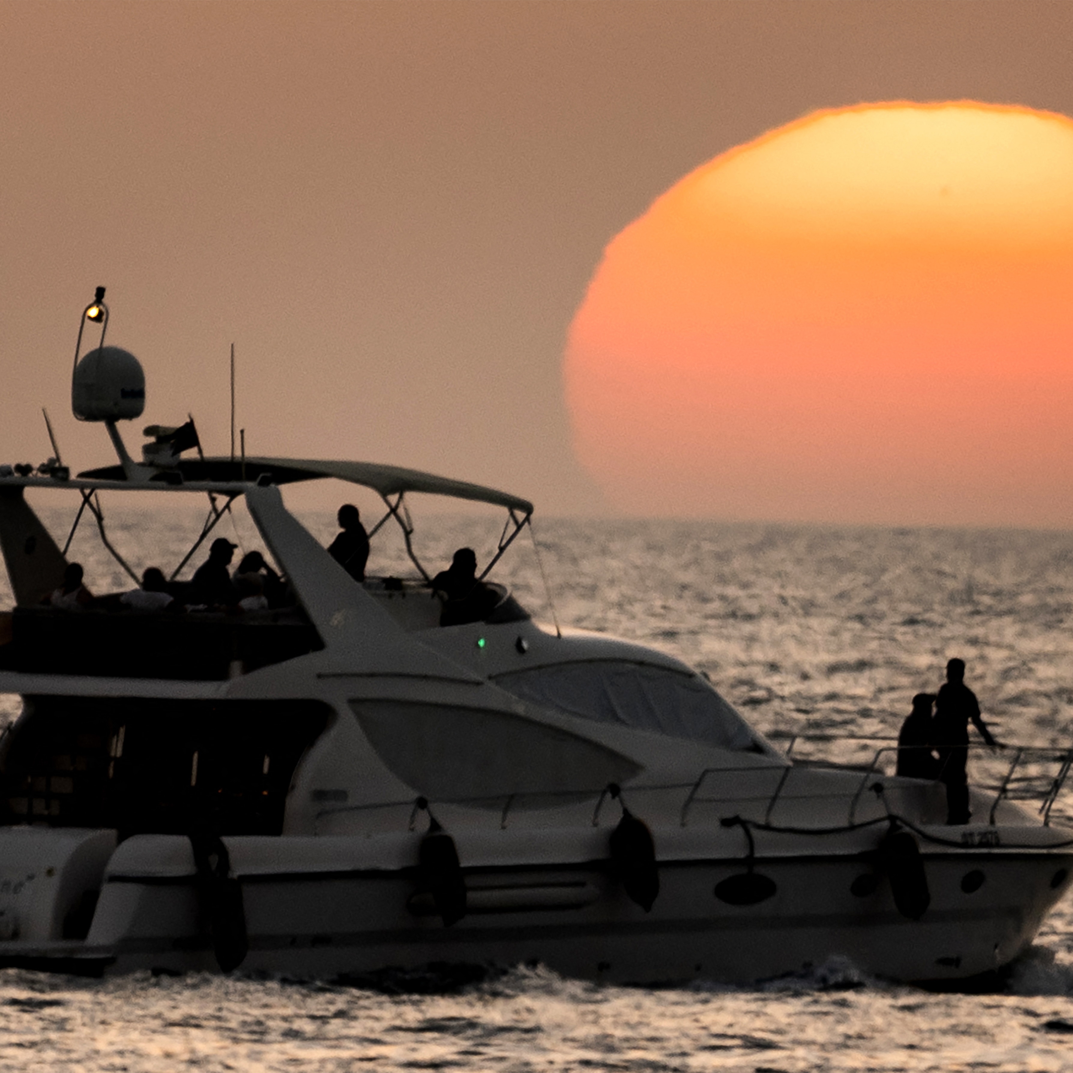 People on a yacht are sihouetted against the setting sun in Dubai, June 11, 2025.
