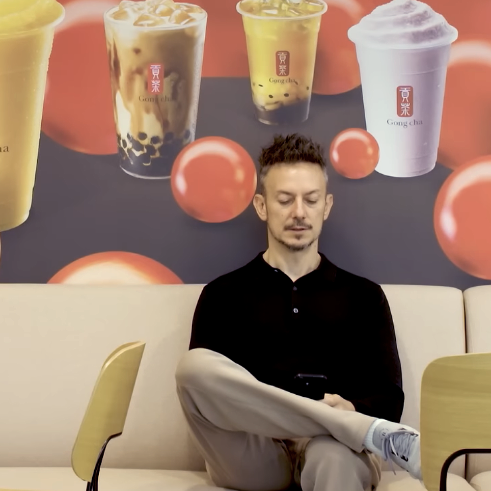 Martin Berry checks his phone while sitting in front of a Gong Cha poster.