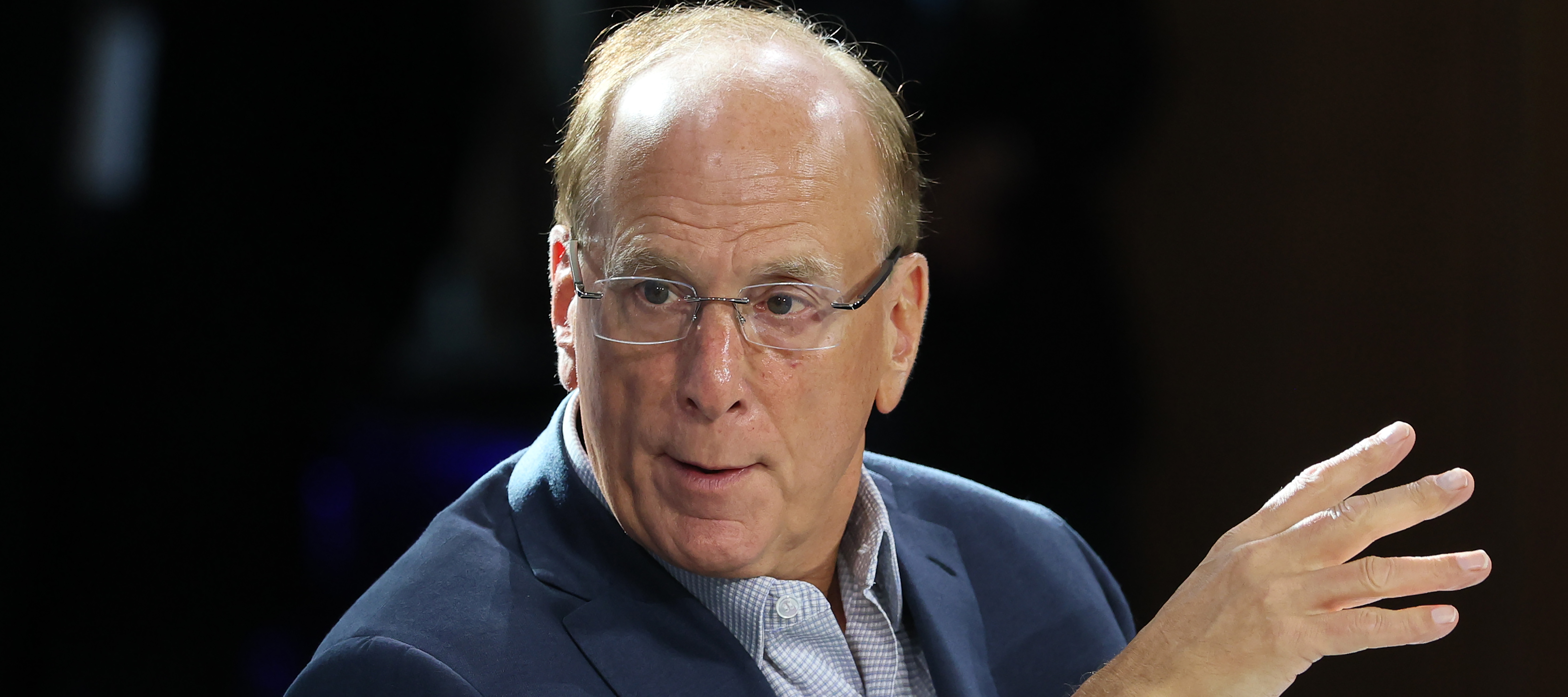 Larry Fink looks over his right shoulder and gestures with one hand, looking concerned.