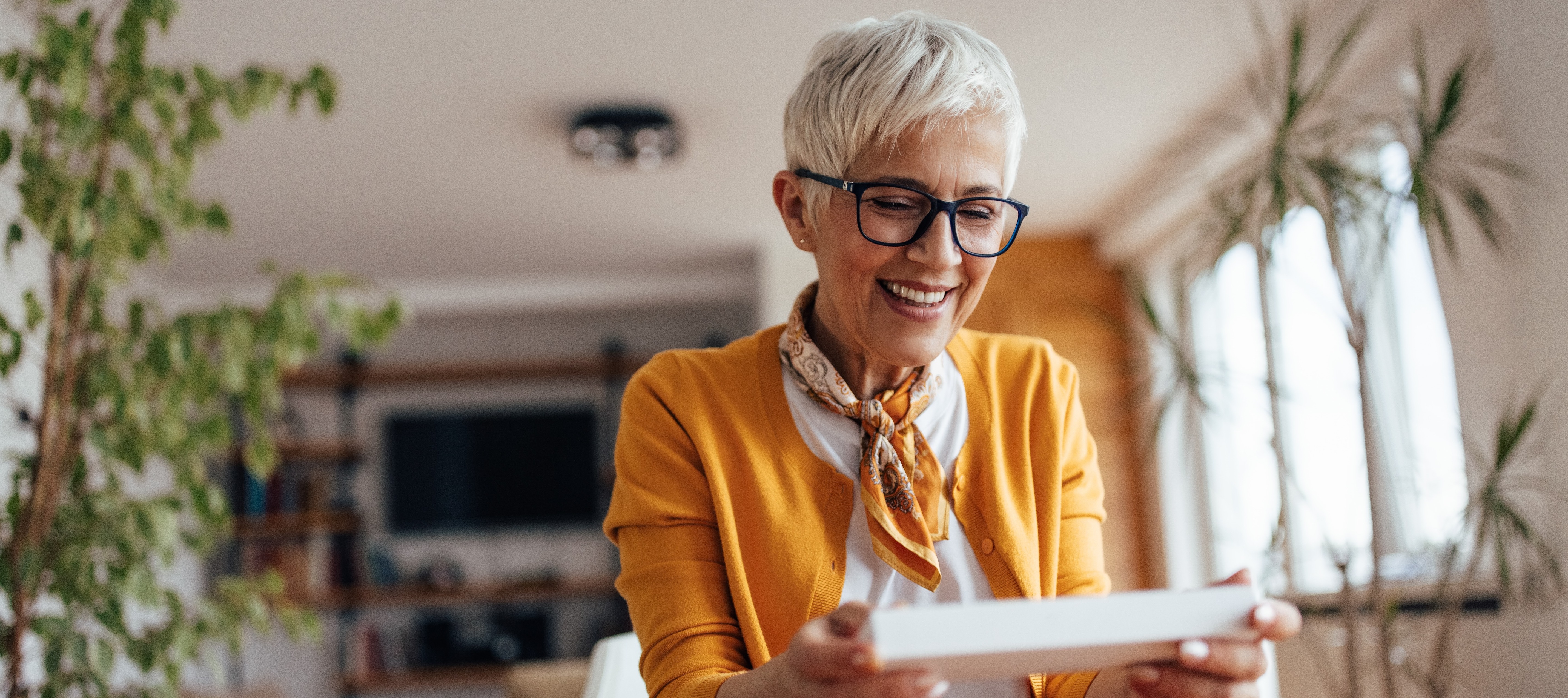 An older woman smiles as she opens a piece of mail in her home.