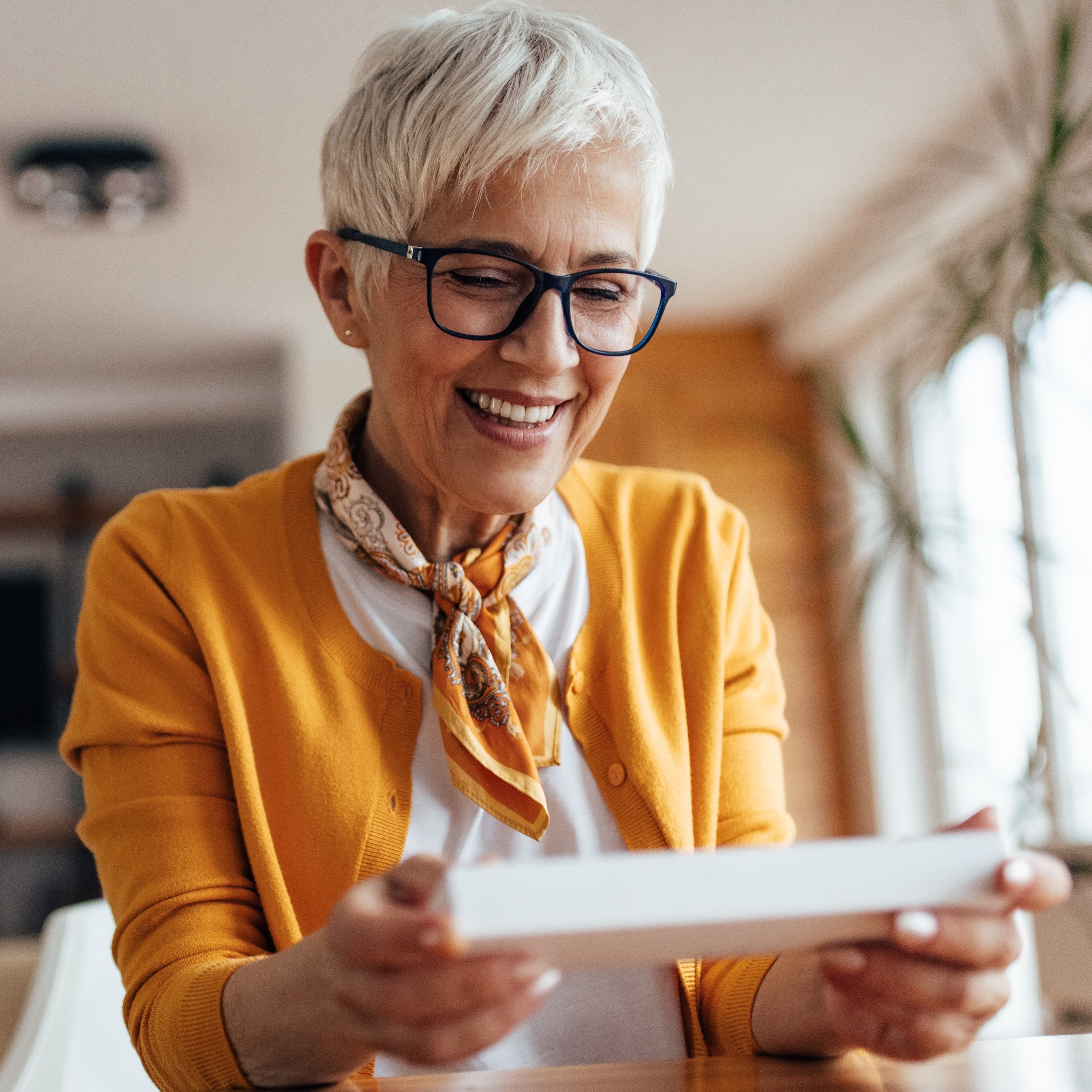 An older woman smiles as she opens a piece of mail in her home.