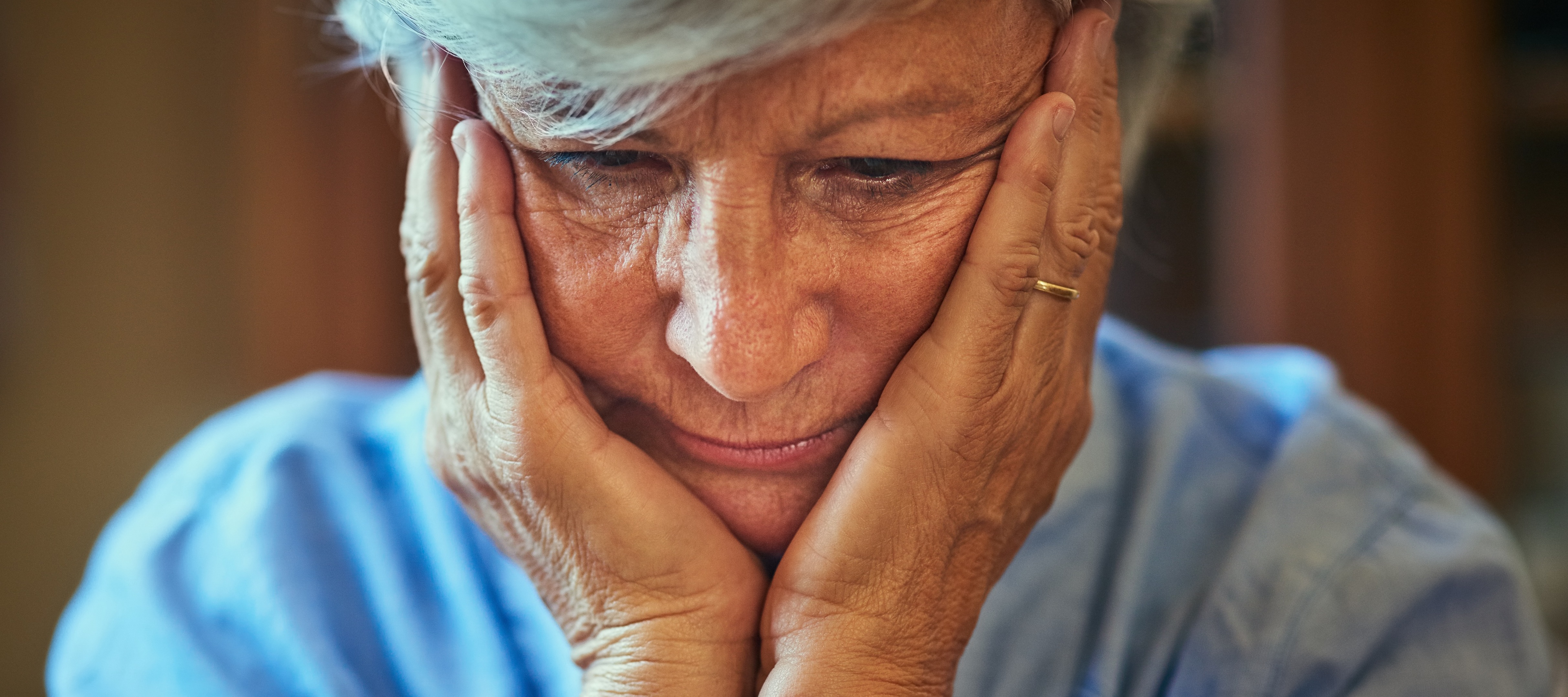 A woman with cropped grey hair holding her face in her hands with worry.